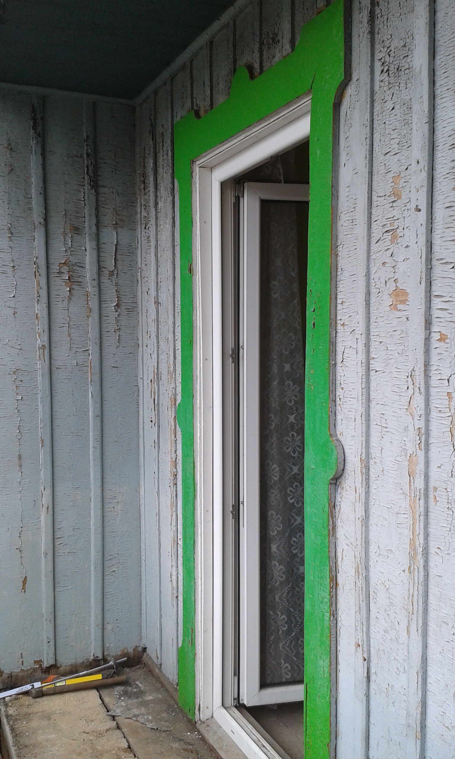 Okno balkonowe w starej drewnianej boazerii z zielonym obramowaniem, przed pracami remontowymi.
