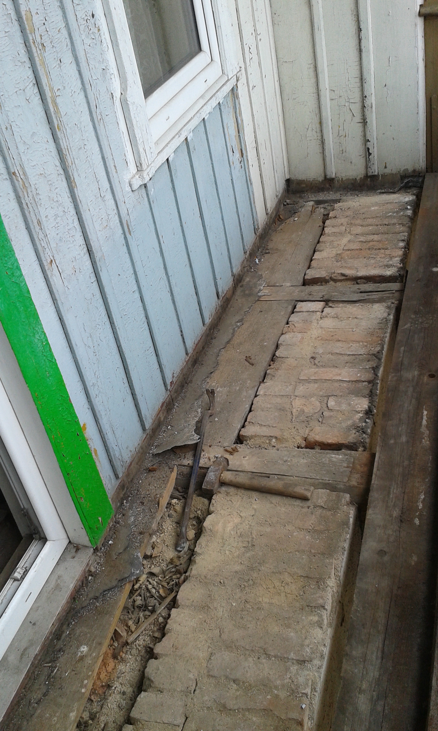 Odsłonięta podłoga przy oknie z widocznymi cegłami, drewnianymi elementami konstrukcyjnymi oraz ubytkami powstałymi podczas prac remontowych.