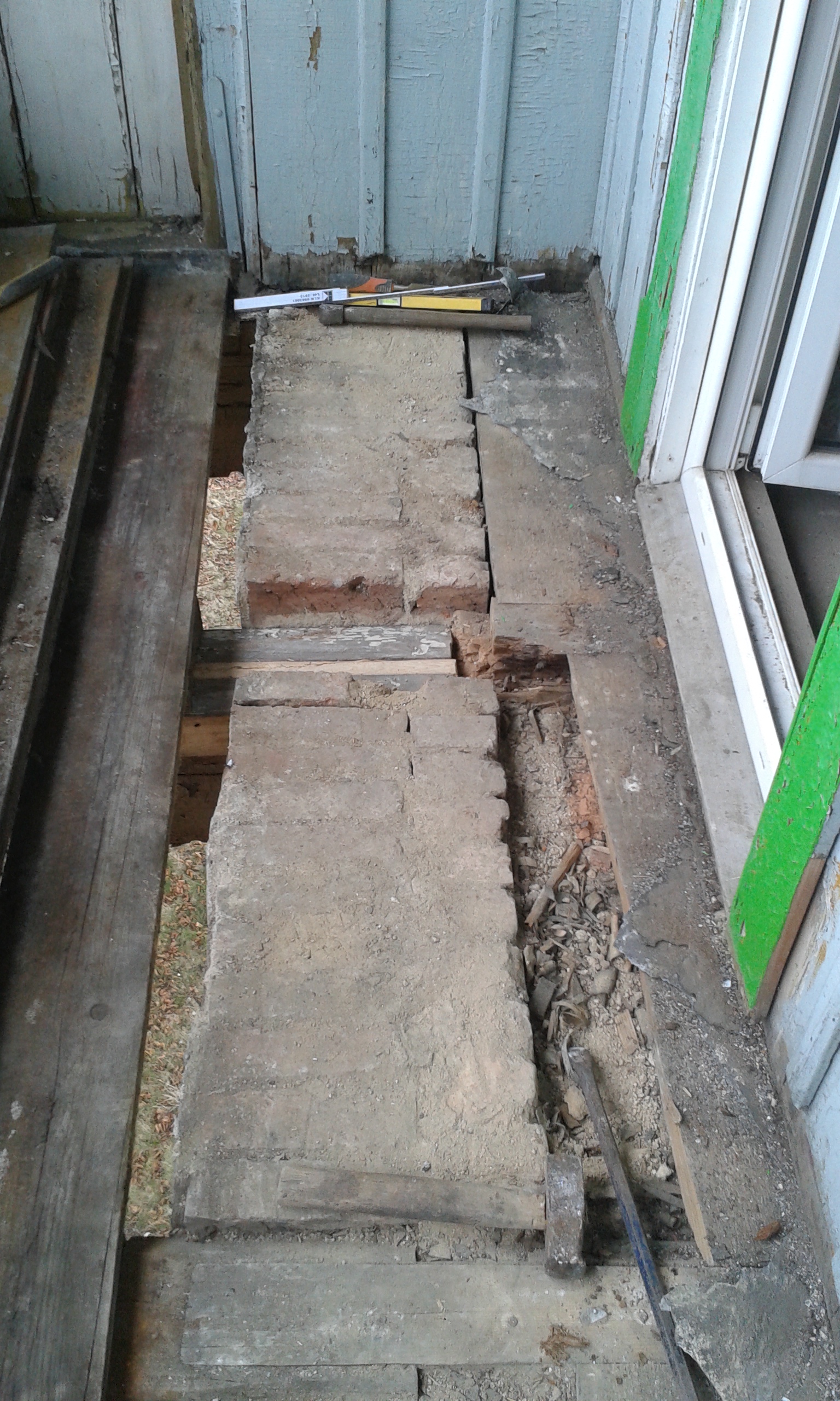 Odsłonięta konstrukcja podłogi z cegły i drewna przy drzwiach balkonowych podczas remontu.