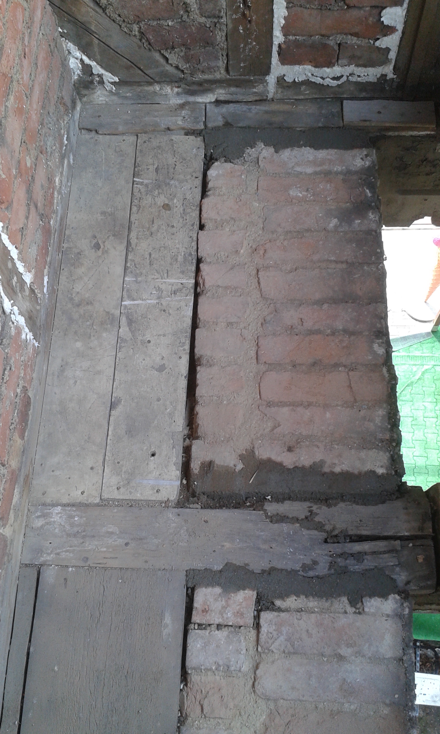 Uzupełniona cegła w konstrukcji stropu balkonu pomiędzy drewnianymi belkami nośnymi, widoczne świeże spoiny po pracach naprawczych.