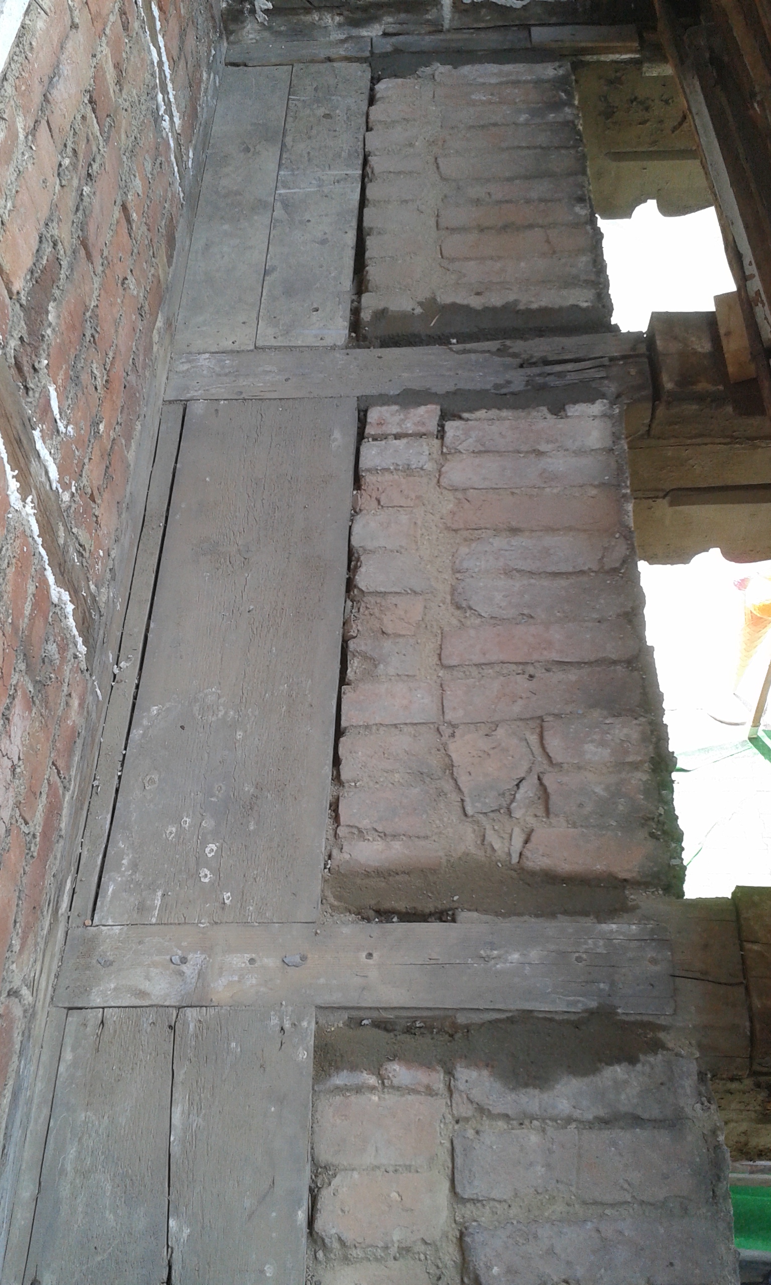 Fragment konstrukcji balkonu z uzupełnioną cegłą, drewnianymi belkami nośnymi i widocznymi miejscami napraw po pracach wzmacniających.