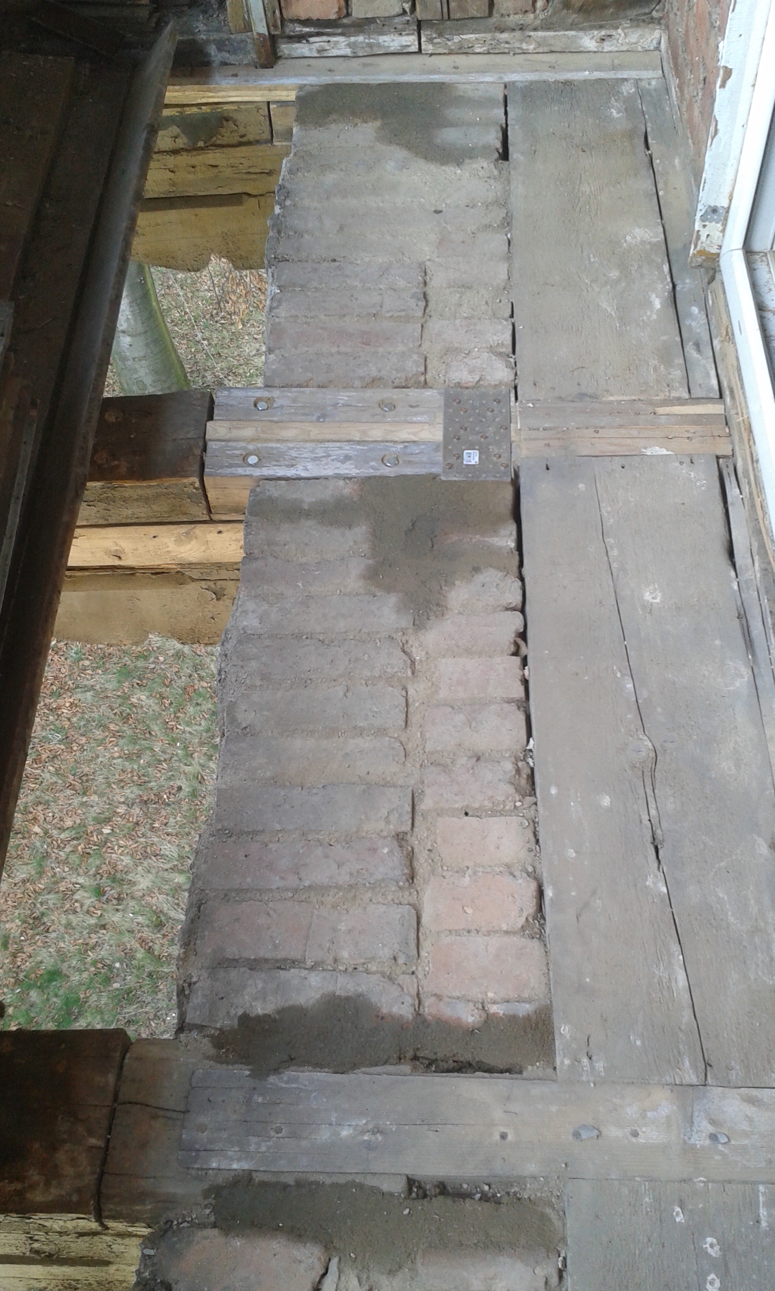 Widok fragmentu konstrukcji balkonu z uzupełnioną cegłą, drewnianymi belkami i metalowymi łącznikami po pracach wzmacniających.