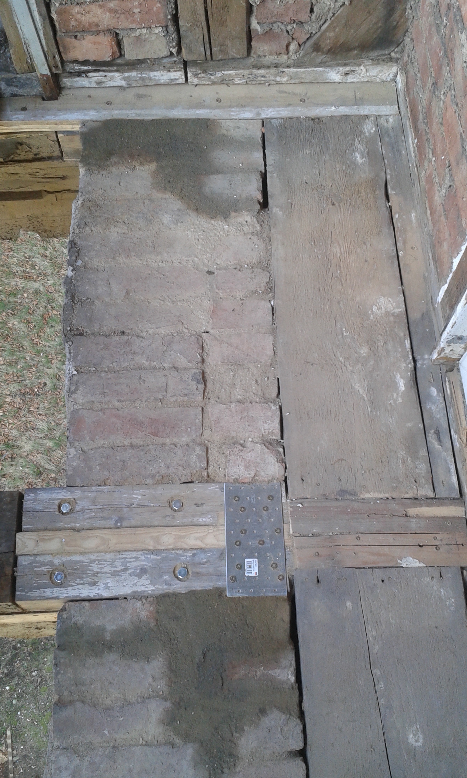 Widok odsłoniętej konstrukcji balkonu z drewnianymi belkami, cegłami i metalowymi łącznikami podczas prac remontowych.