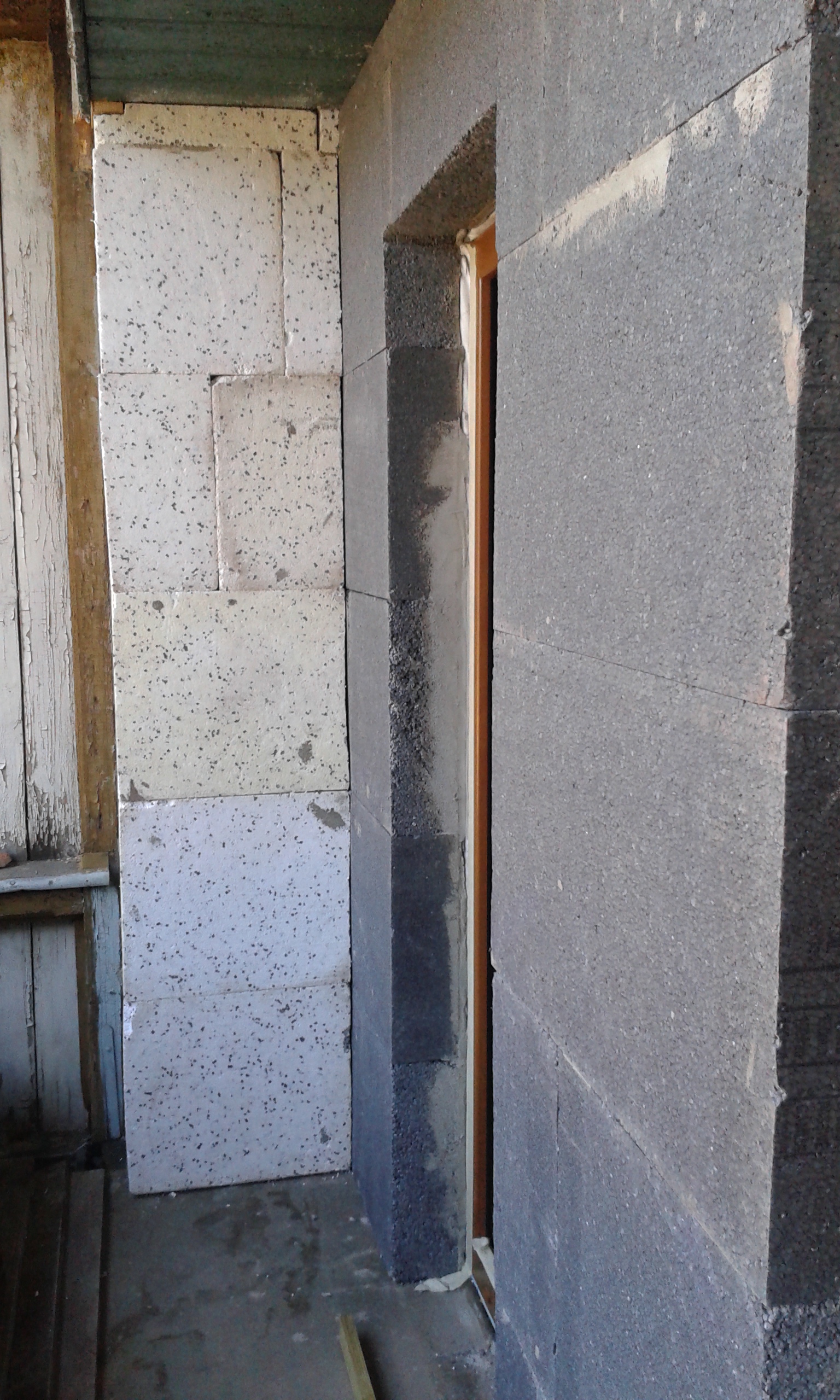 : Boczne ościeże balkonu z osadzonym oknem, widoczne warstwy grafitowego styropianu oraz jasnego styropianu w trakcie ocieplania.