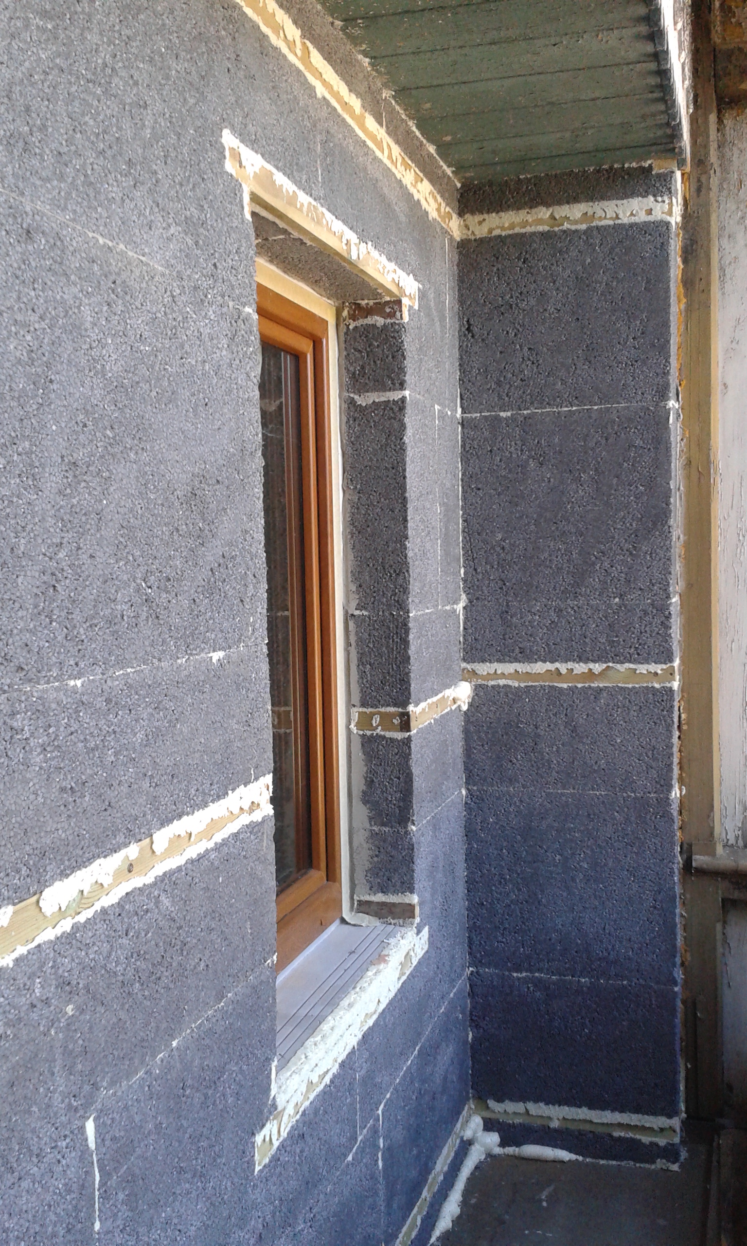 Ściana balkonu w trakcie ocieplania styropianem grafitowym, z osadzonym oknem i widocznymi warstwami kleju wokół ościeży oraz na łączeniach płyt.