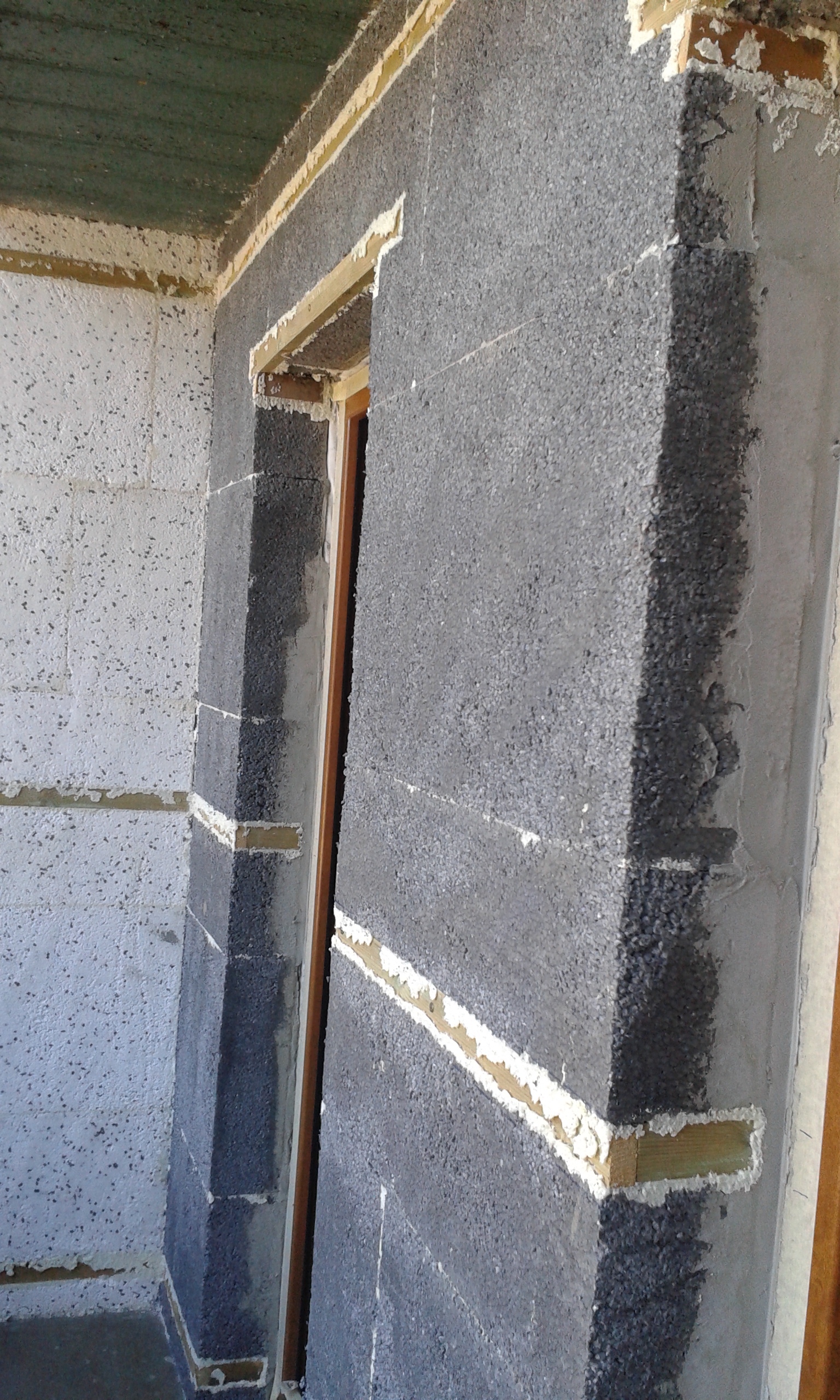 Ościeże okna balkonowego w trakcie docieplania styropianem grafitowym, z widocznymi warstwami kleju i niedokończonym wykończeniem wokół ramy okiennej.