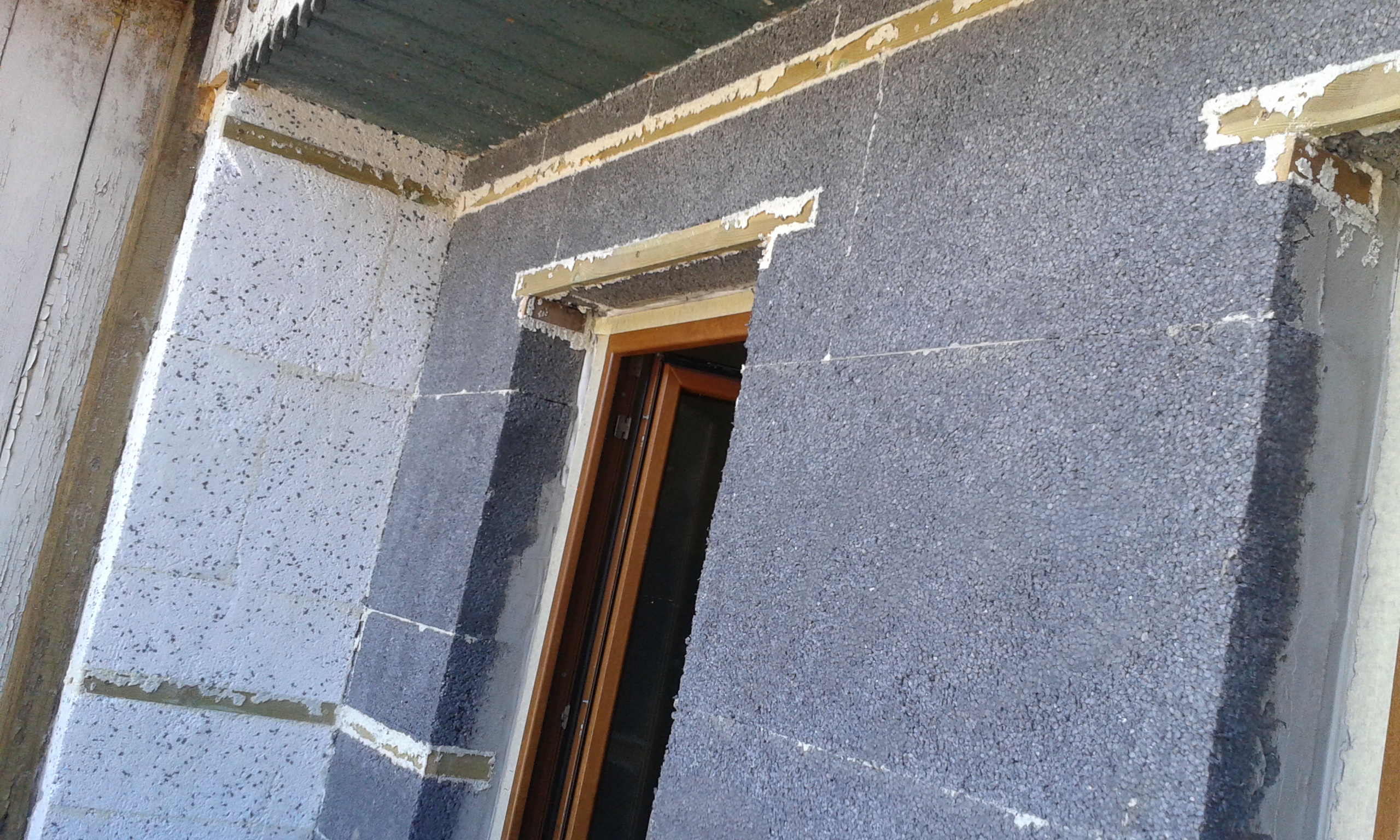 Ściana balkonowa w trakcie docieplania styropianem, z widocznym otworem okiennym i fragmentami kleju montażowego wokół ramy okna.