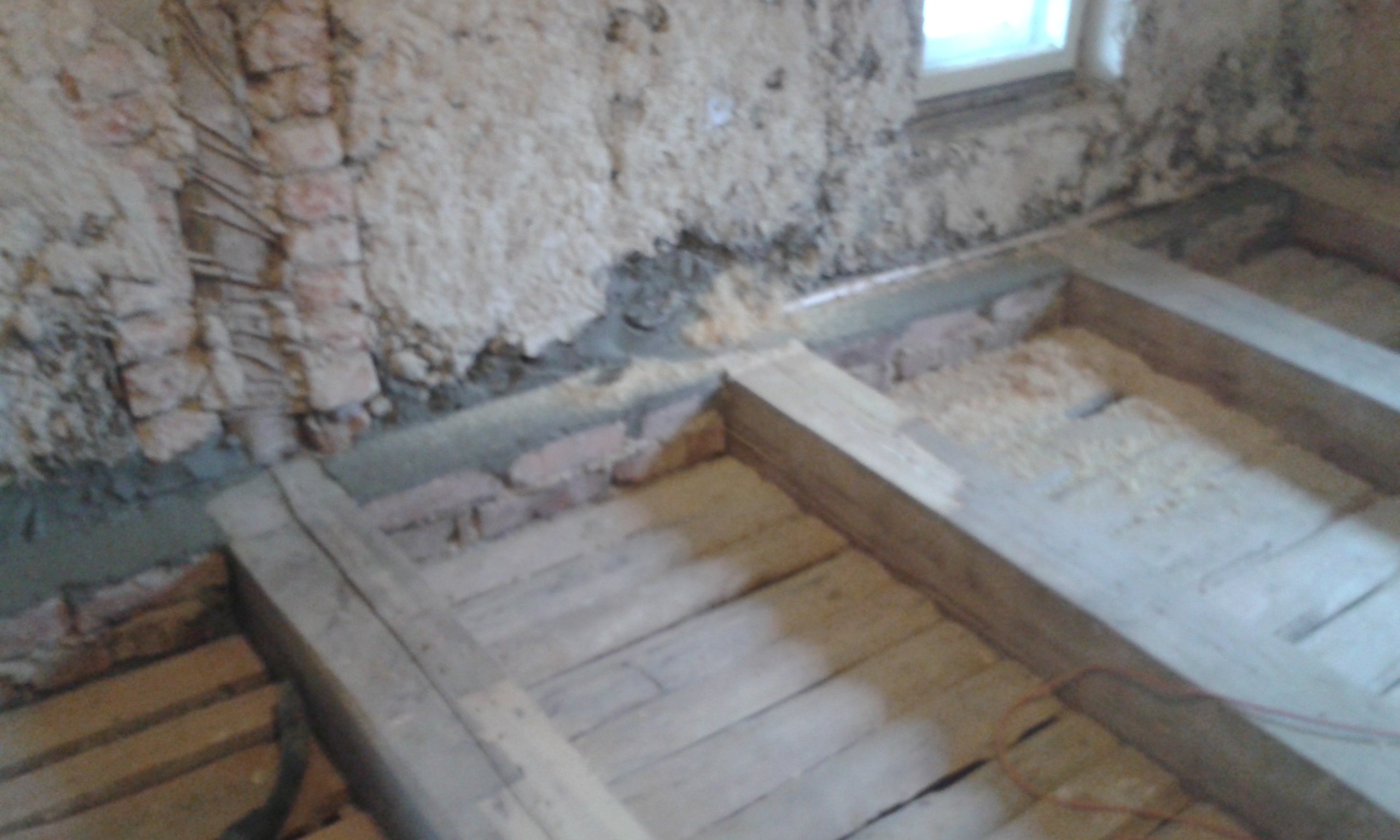 Fragment odkrytego stropu drewnianego przy ścianie z oknem, widoczne belki konstrukcyjne oraz ślady prowadzonych prac remontowych.