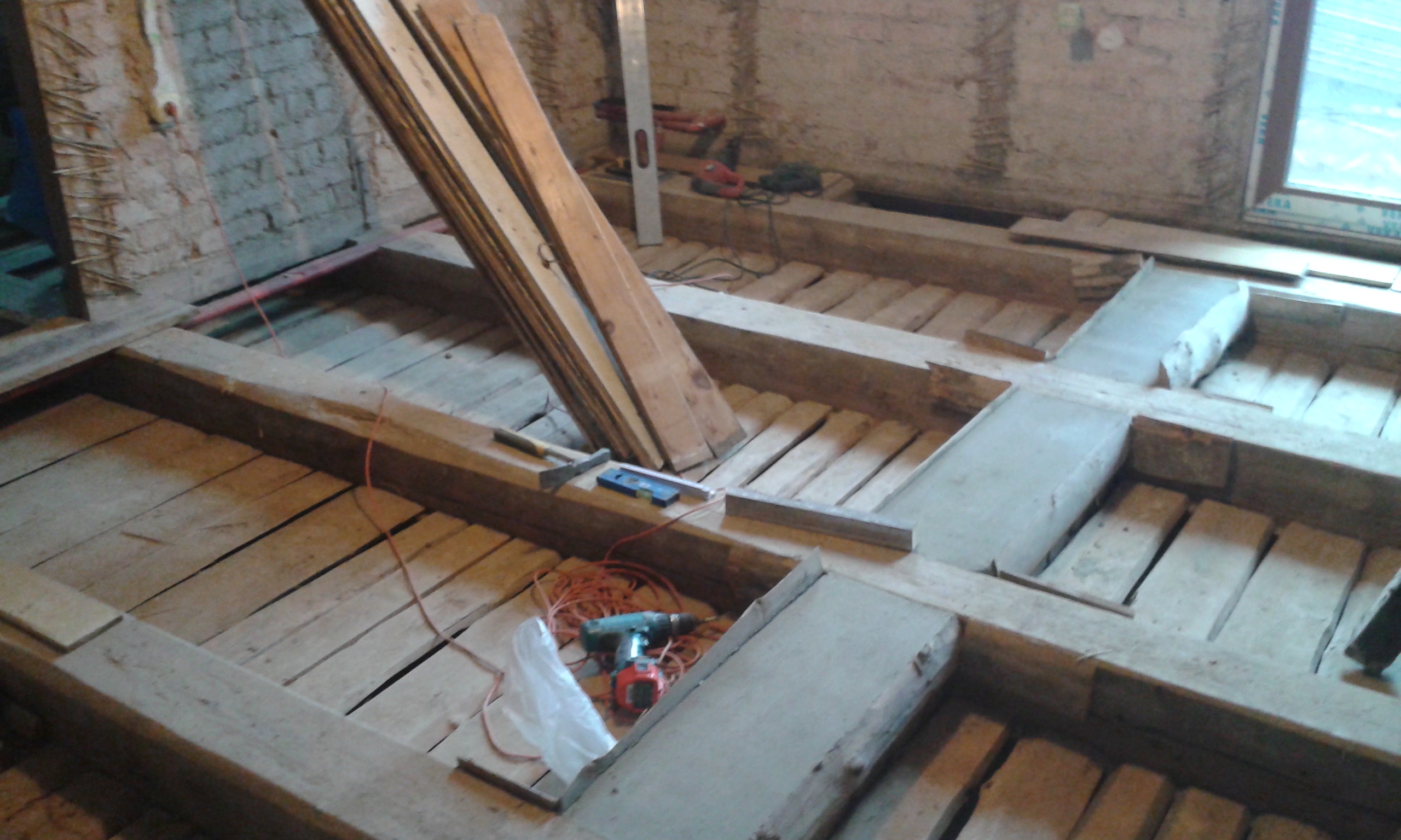 Widok na odkrytą konstrukcję drewnianego stropu z belkami, narzędziami oraz elementami konstrukcyjnymi w trakcie prac remontowo-budowlanych.