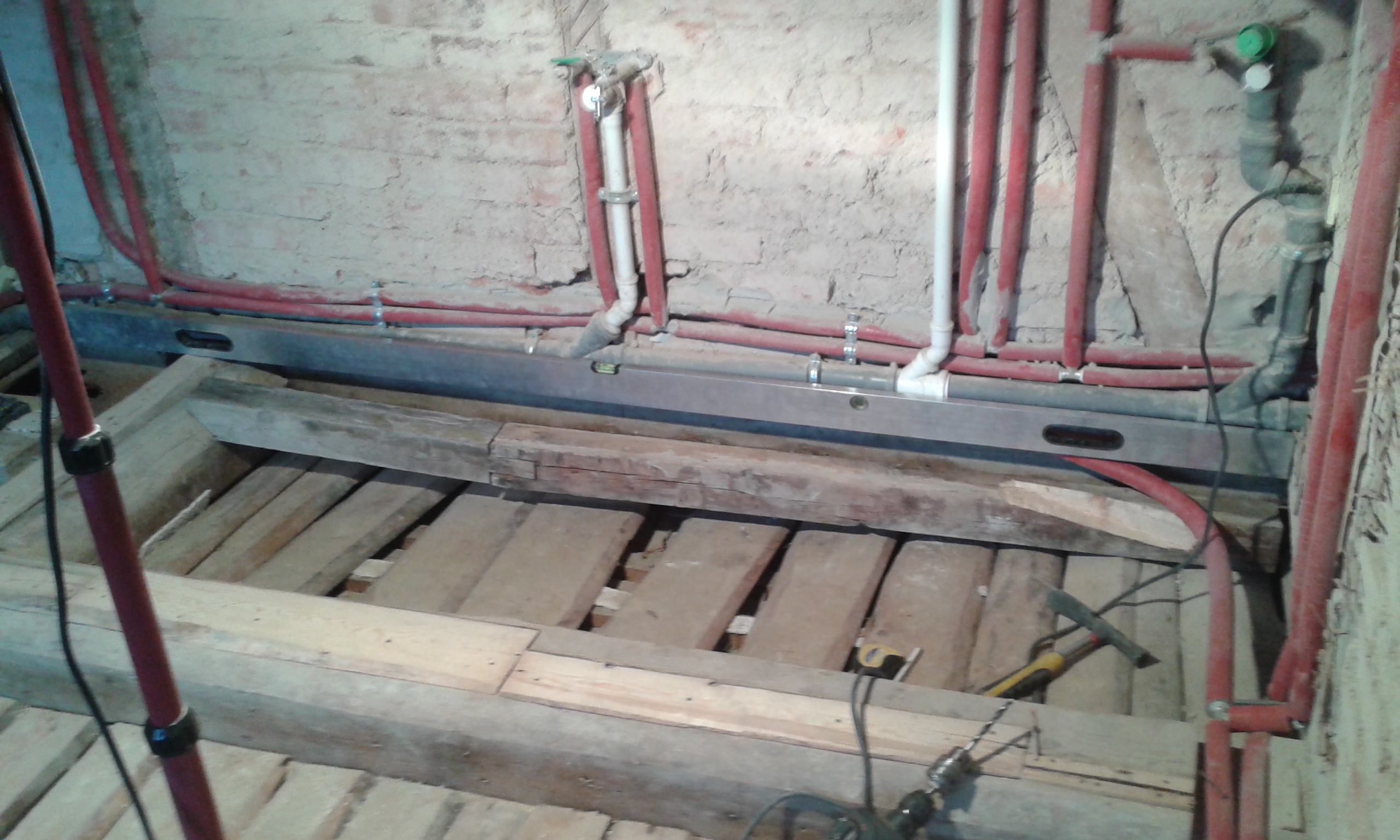 Odkryty strop drewniany z belkami i deskami, widoczny poziomica oraz instalacje hydrauliczne prowadzone przy ścianie podczas prac remontowych.