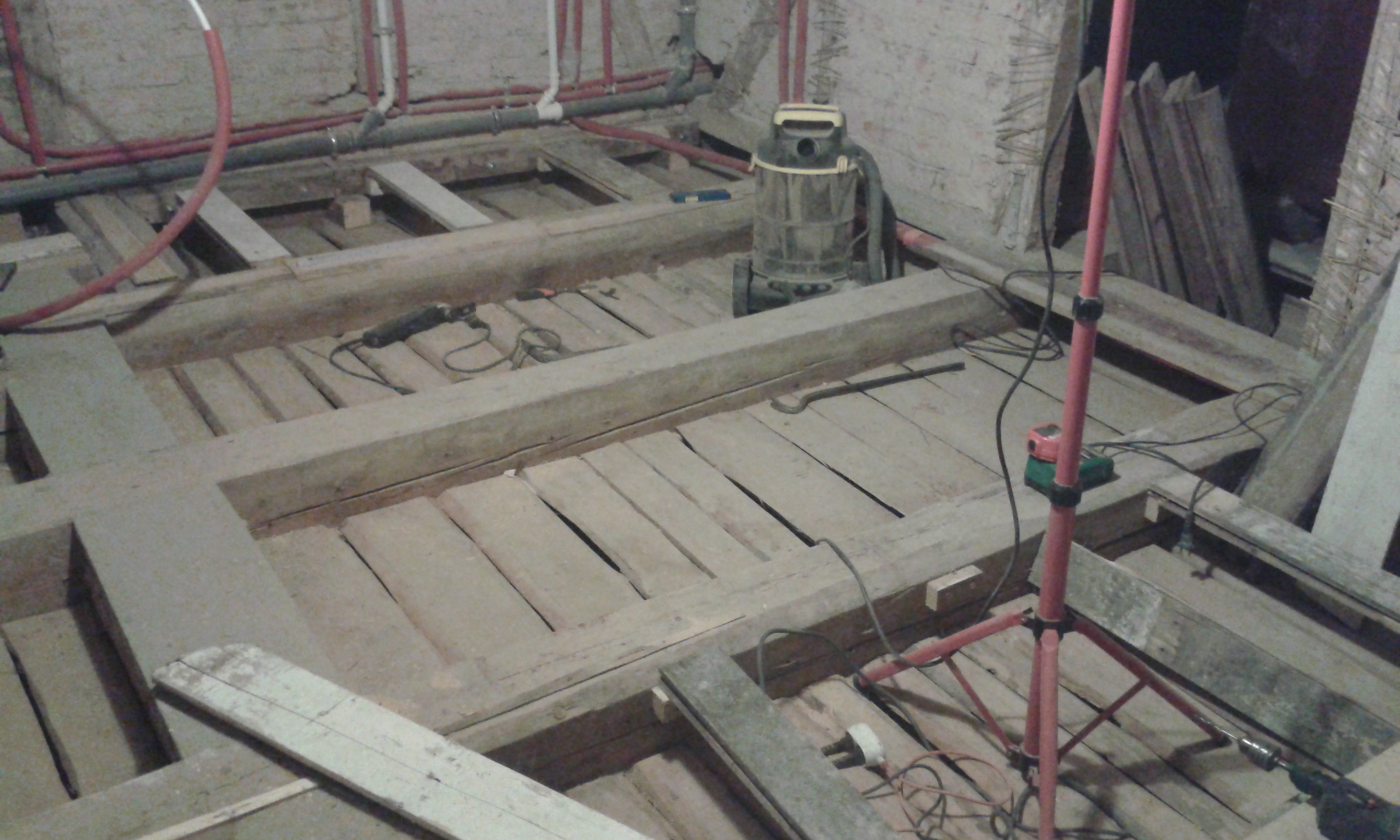 Widok na odkryty strop drewniany z belkami, prowadzonymi instalacjami oraz sprzętem budowlanym w trakcie prac modernizacyjnych.