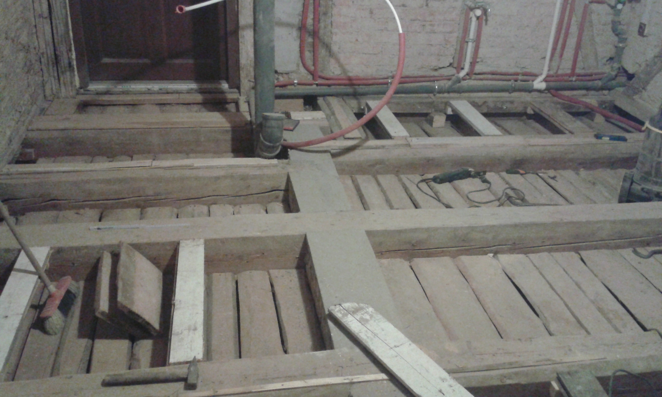 Wnętrze z odkrytą konstrukcją stropu, widocznymi belkami drewnianymi, instalacjami hydraulicznymi oraz narzędziami podczas prac remontowych.