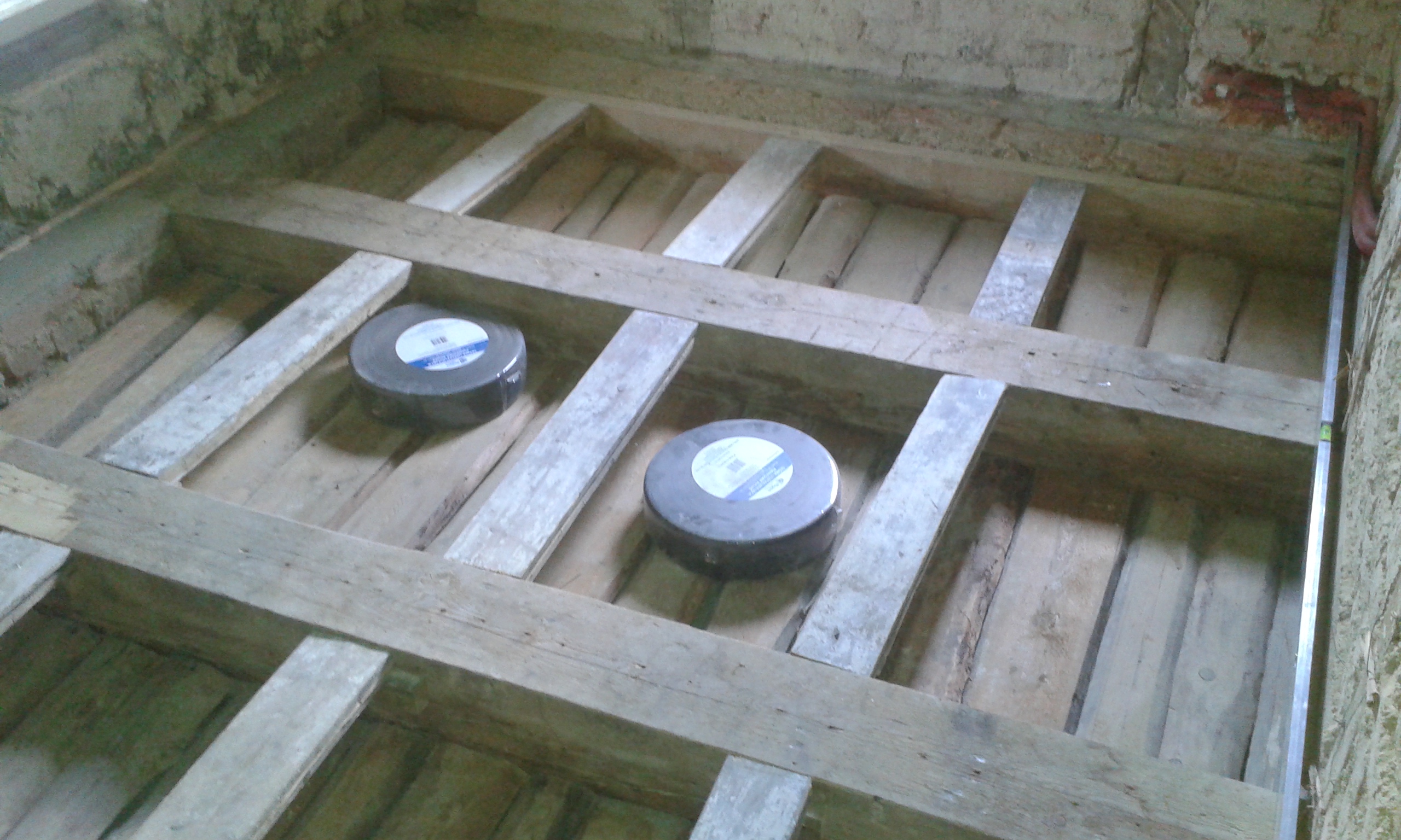 Widok na odkryty strop z drewnianymi belkami i listwami montażowymi, przygotowany do wykonania izolacji oraz kolejnych etapów prac budowlanych.