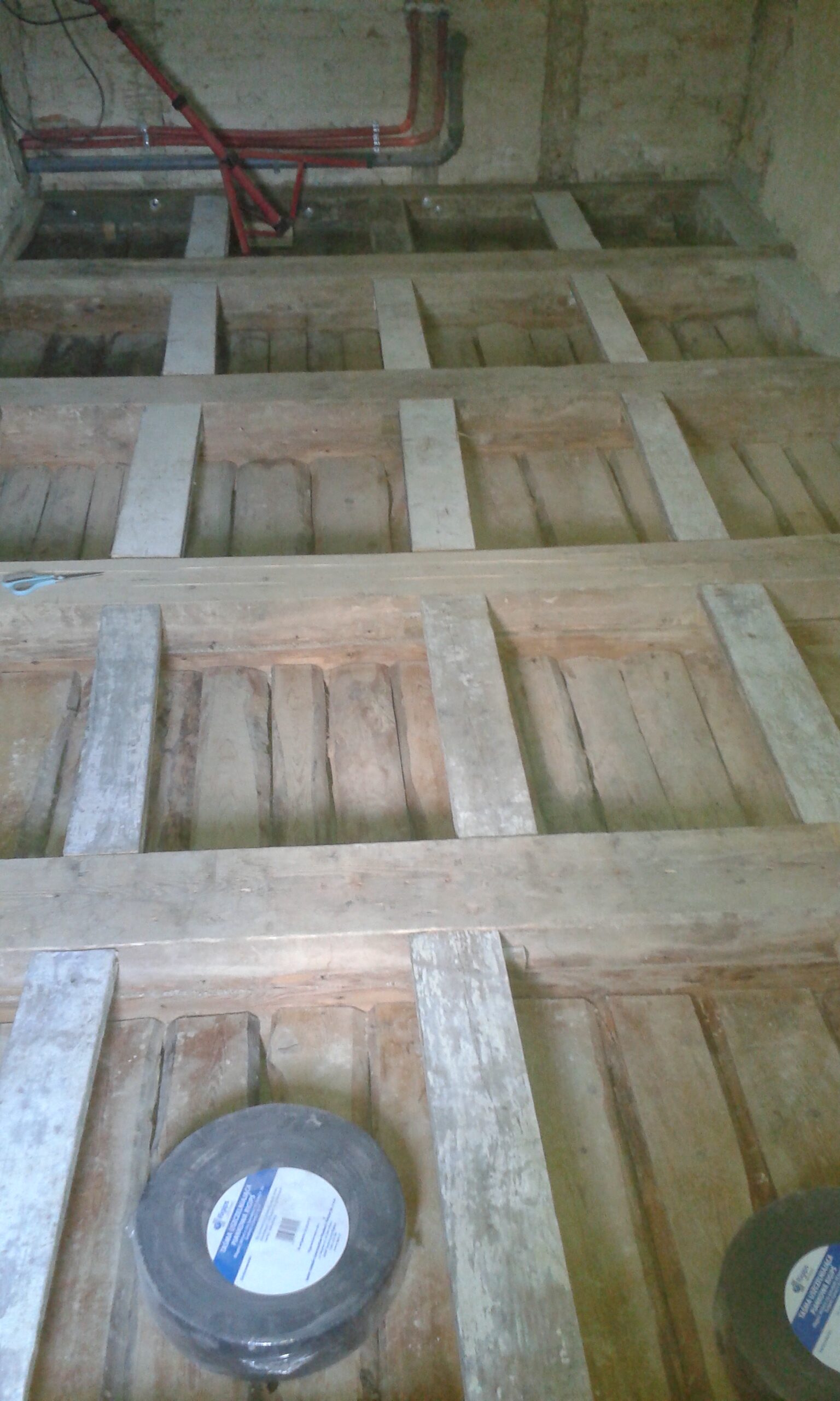 Odkryta konstrukcja drewnianego stropu z widocznymi belkami, listwami montażowymi oraz instalacją prowadzoną przy ścianie w trakcie prac budowlanych.