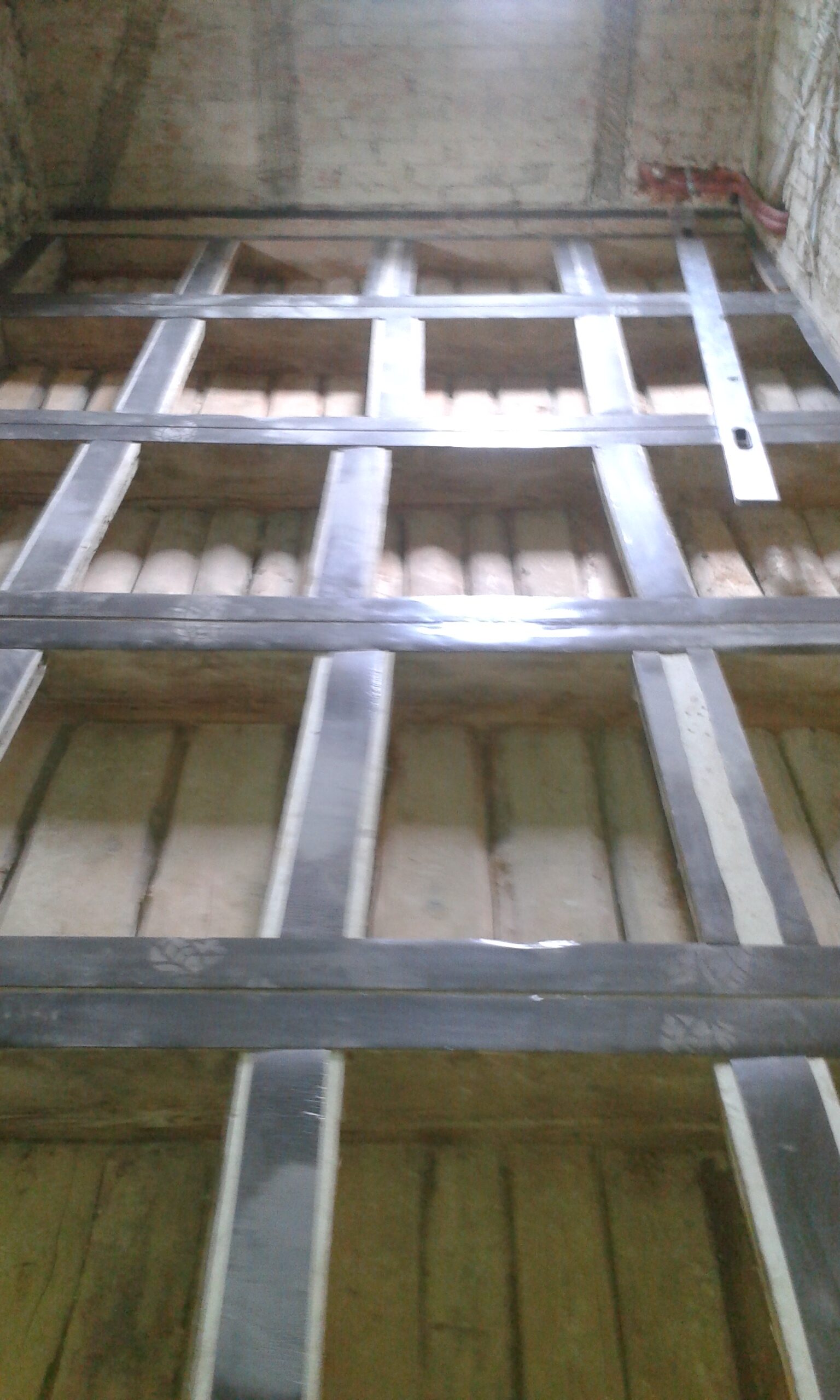 Widok na strop poddasza z zamontowanym rusztem konstrukcyjnym z profili, przygotowanym pod ułożenie izolacji i dalsze warstwy podłogi.