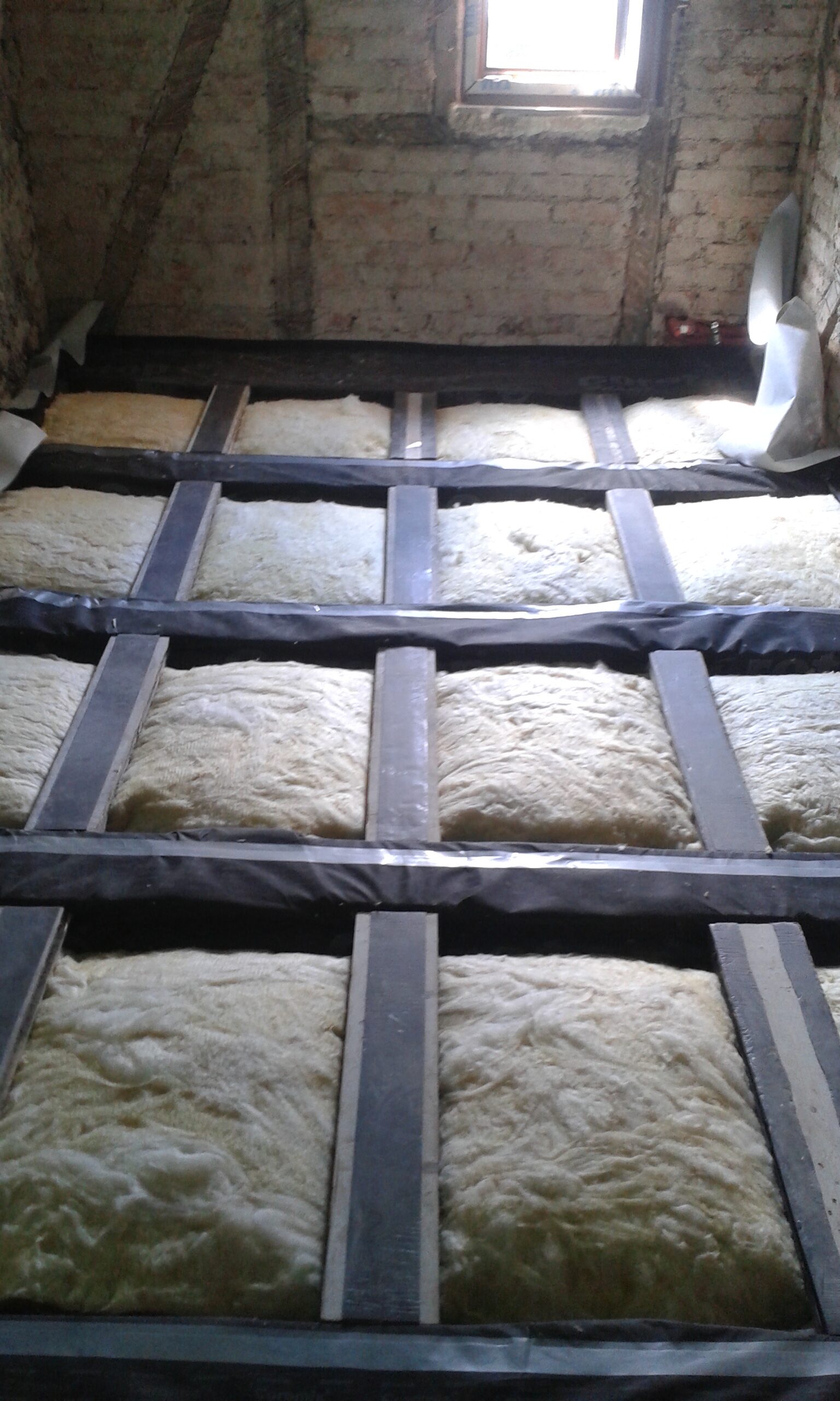 Poddasze z widoczną konstrukcją stropu i ułożoną izolacją termiczną między belkami, przygotowane do montażu płyt podłogowych.