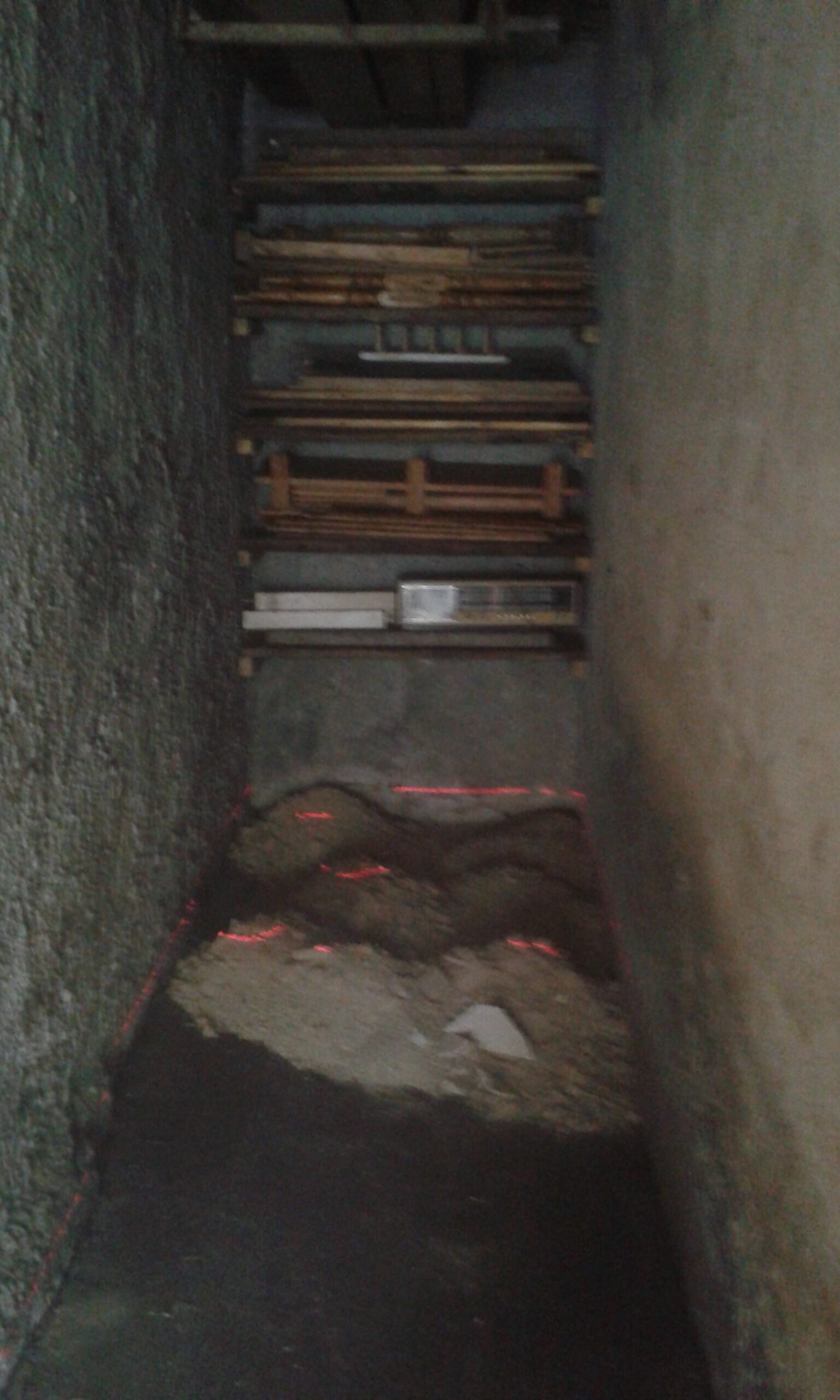 Wąskie pomieszczenie w trakcie przygotowania podłoża pod kostkę brukową, z naniesionymi liniami poziomowania i widocznym materiałem do wyrównania nawierzchni.