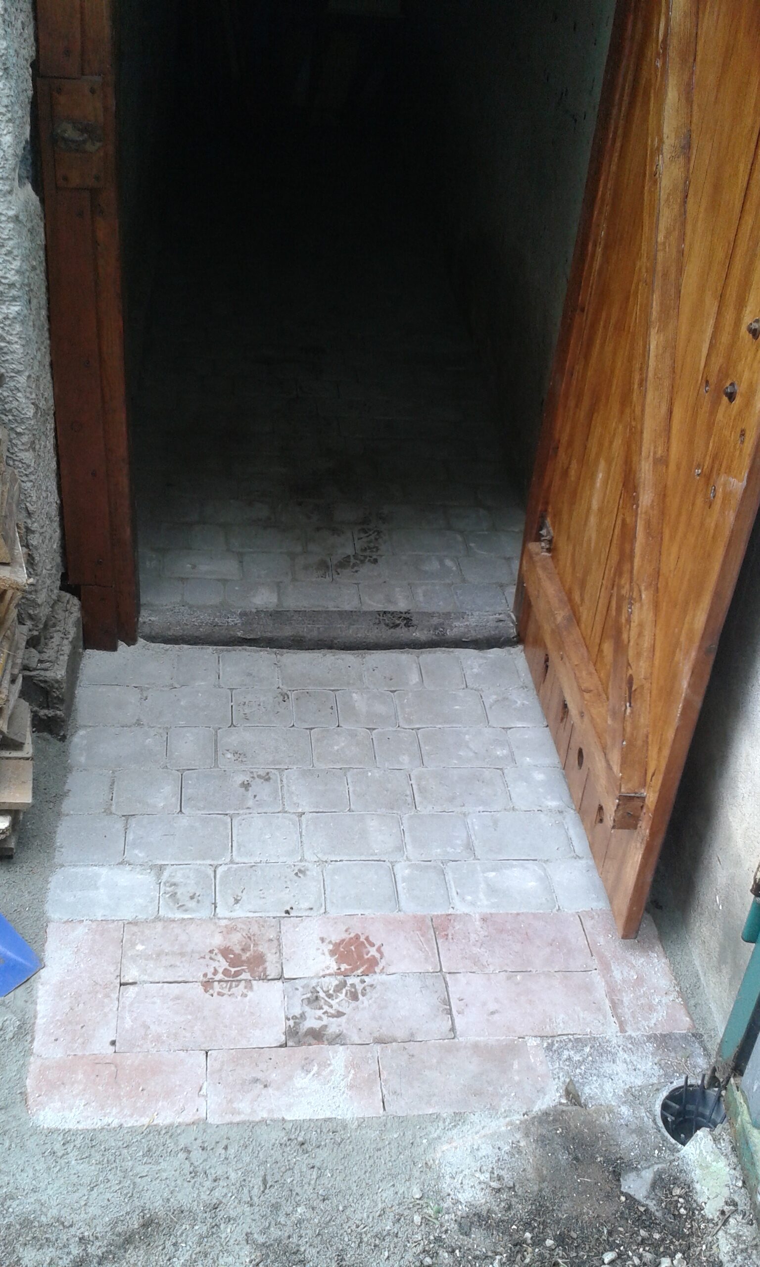 Widok na wejście do pomieszczenia z nowo ułożoną kostką brukową, pokazujący estetyczne wykończenie progu i dopasowanie nawierzchni do drzwi.