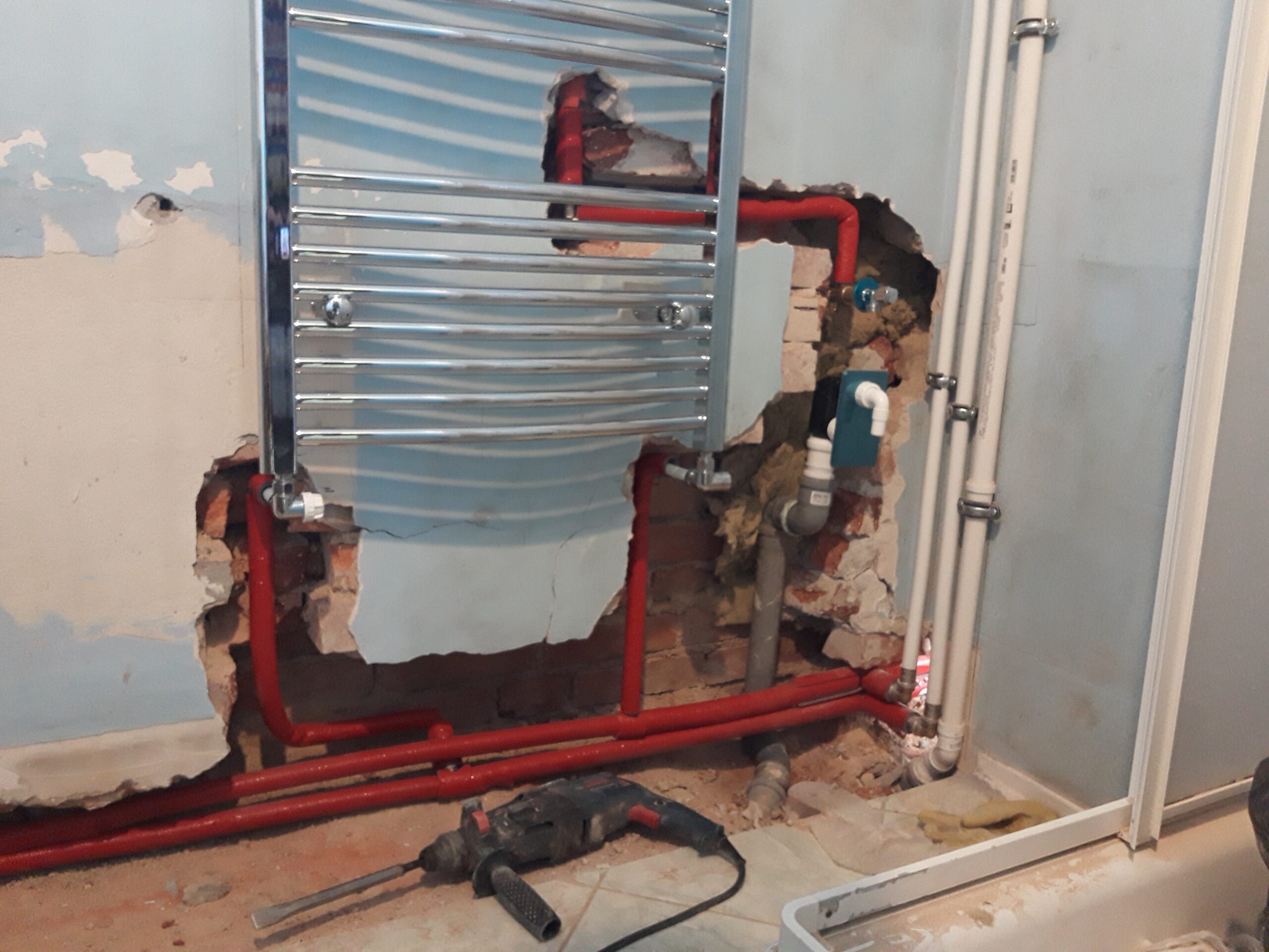 Fragment łazienki podczas remontu z widocznym grzejnikiem drabinkowym, odsłoniętymi rurami grzewczymi oraz elementami instalacji przygotowanymi do zabudowy.