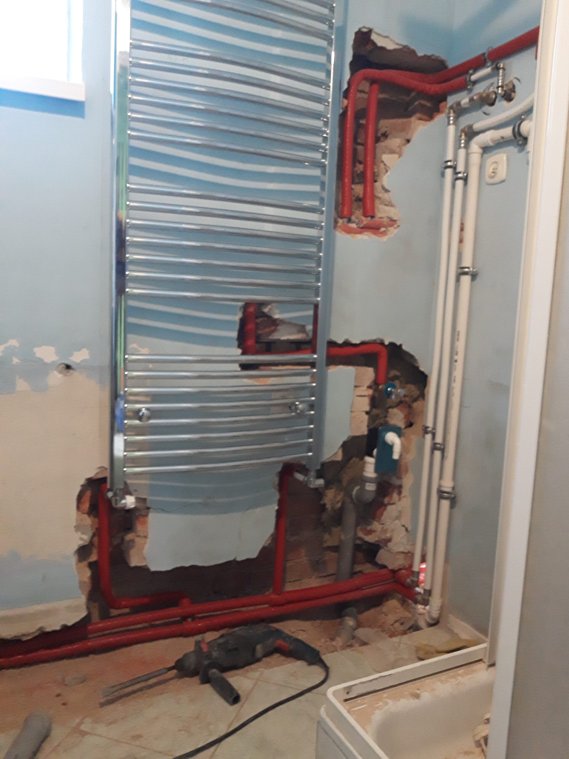 Łazienka w trakcie remontu z zamontowanym grzejnikiem drabinkowym oraz odsłoniętą instalacją grzewczą i wodną przygotowaną do zabudowy.