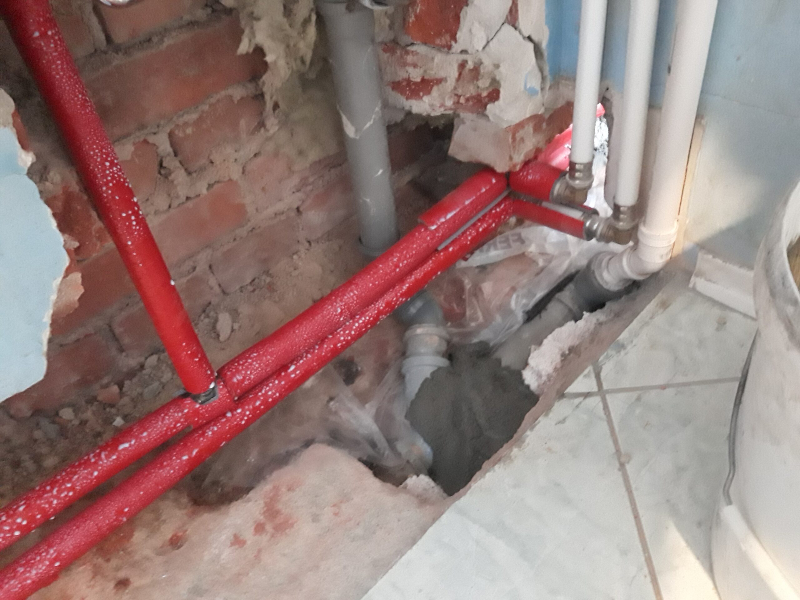Odsłonięte rury instalacji wodnej i kanalizacyjnej w podłodze łazienki, pokazujące przebieg przewodów podczas prac remontowych.