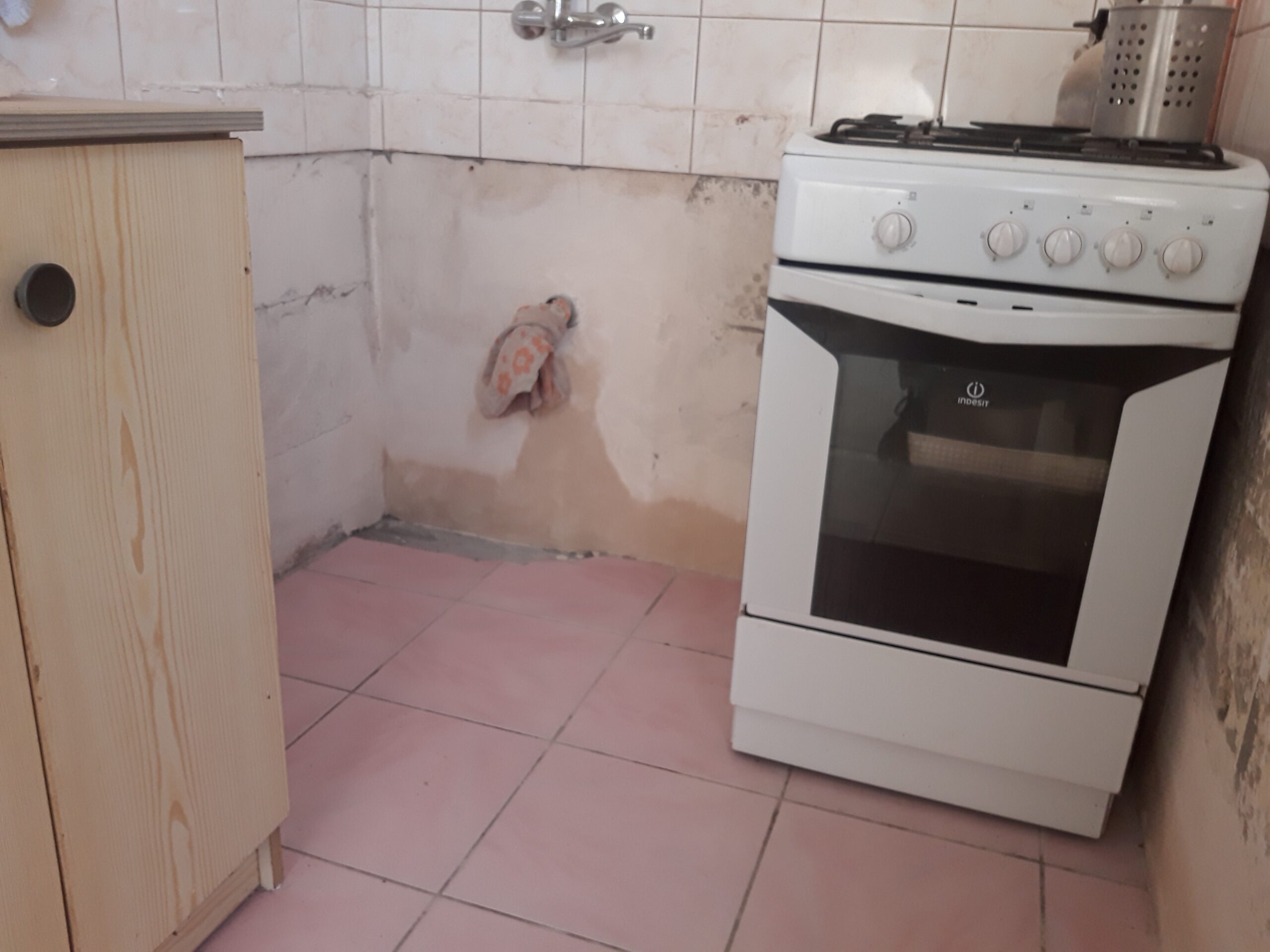 Fragment kuchni w trakcie prac remontowych z widoczną kuchenką gazową, zdjętymi elementami instalacji i nieukończonym wykończeniem ścian oraz podłogi.