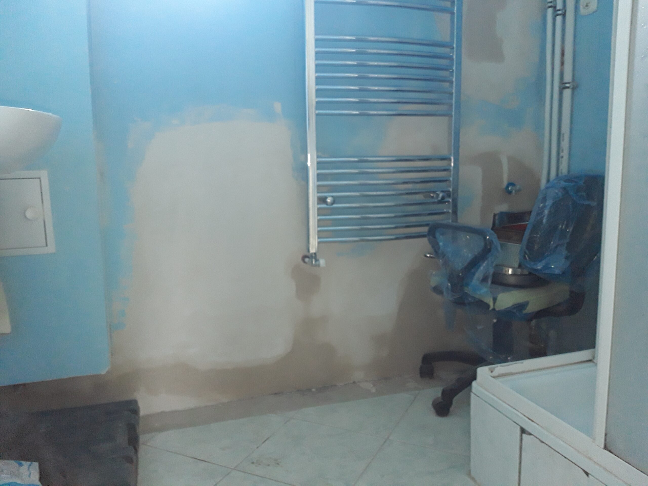 Łazienka w trakcie prac remontowych z widocznym grzejnikiem drabinkowym, nieukończonymi ścianami i elementami wyposażenia zabezpieczonymi folią.