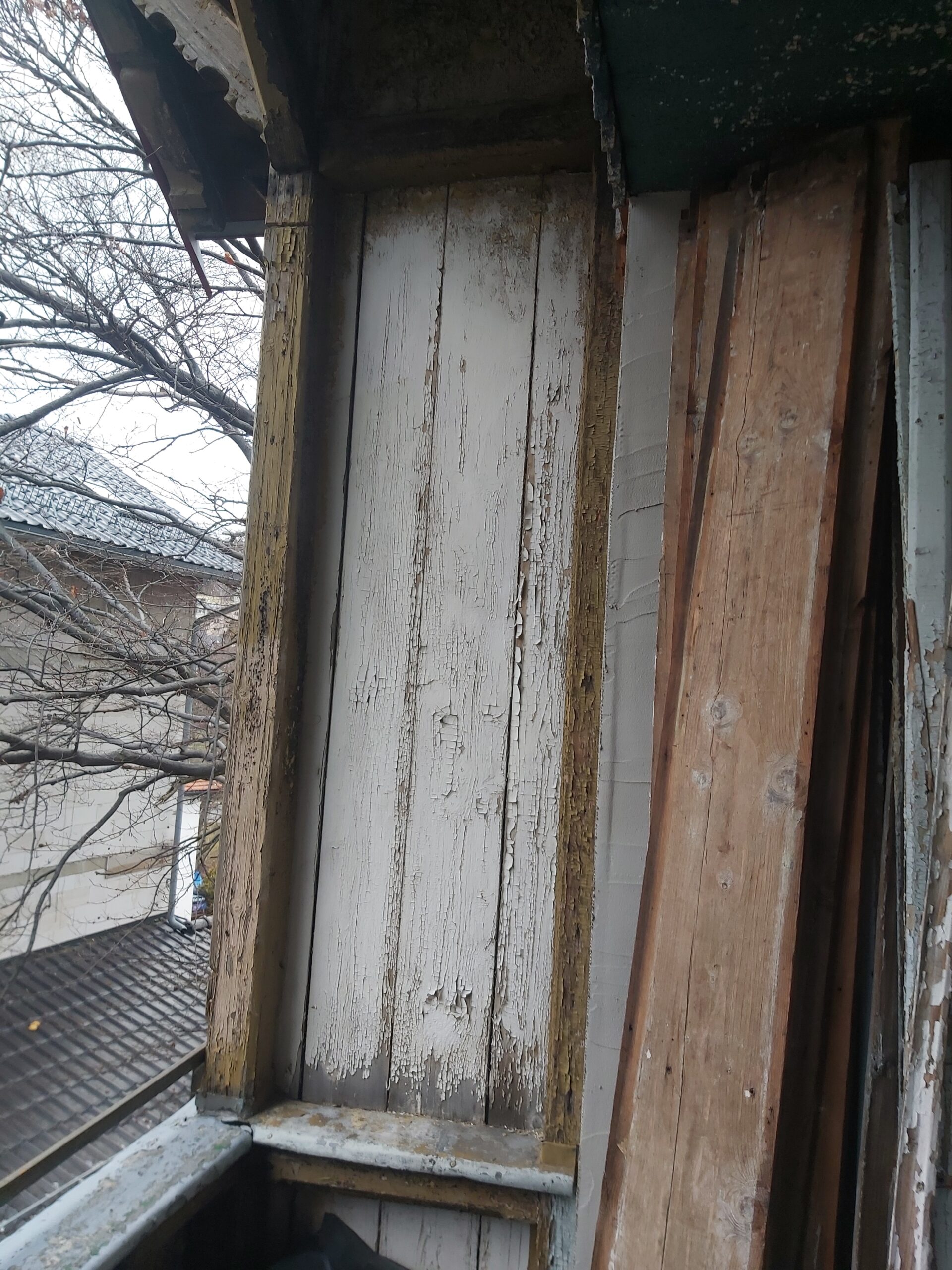 Odsłonięte ościeże okna z widocznymi starymi, zniszczonymi deskami drewnianymi oraz śladami wcześniejszych powłok, przygotowane do renowacji.