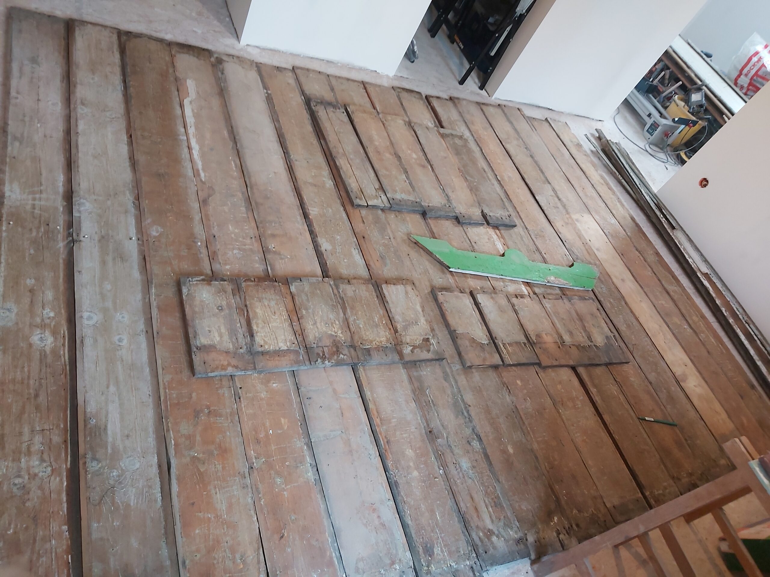 Odsłonięta stara podłoga z drewnianych desek po demontażu warstw wykończeniowych, widoczne ślady użytkowania oraz przygotowanie do dalszych prac remontowych.