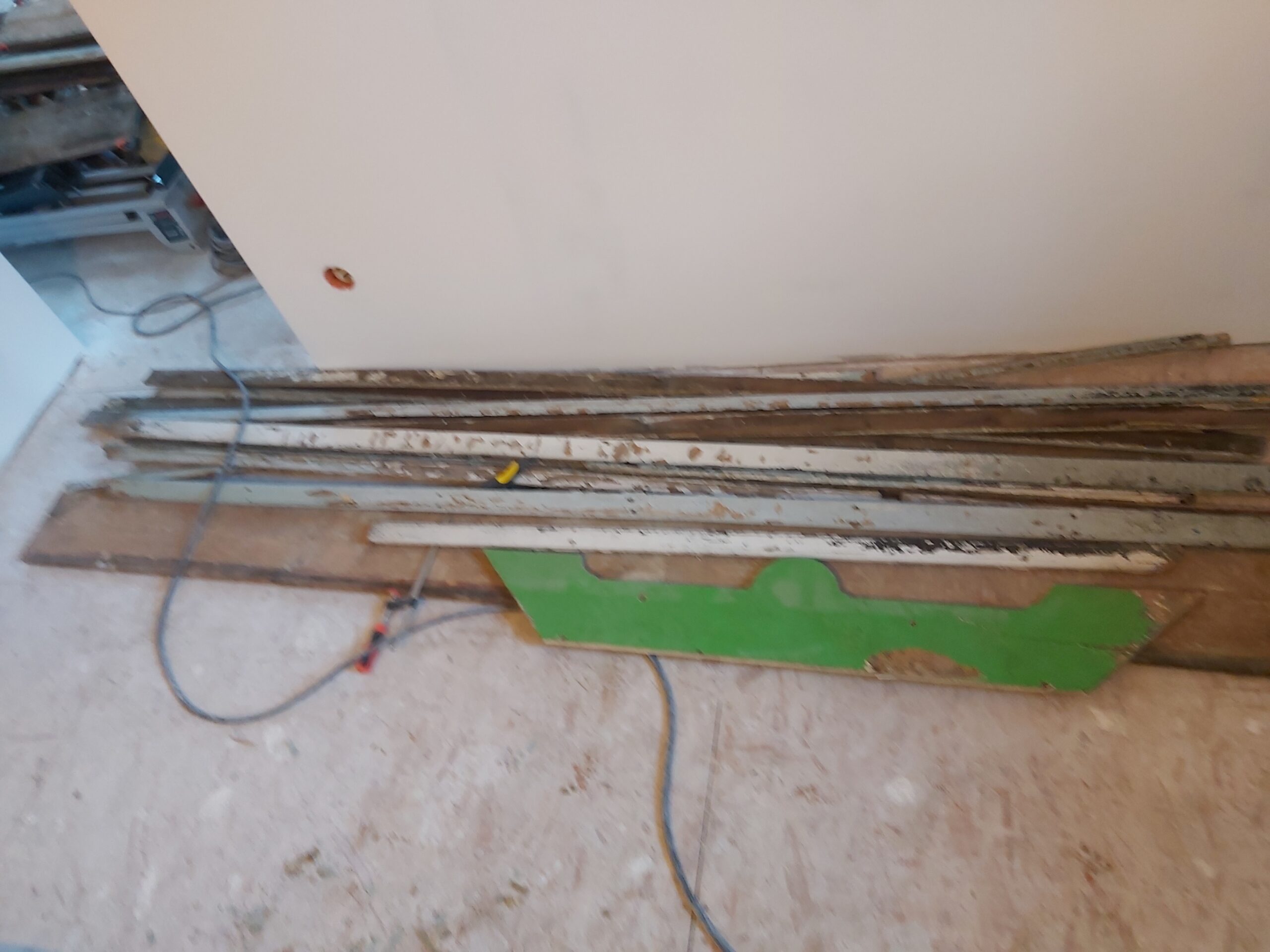 Zdemontowane stare listwy i elementy drewniane ułożone przy ścianie, widoczne przewody oraz przygotowanie do dalszych prac remontowych.