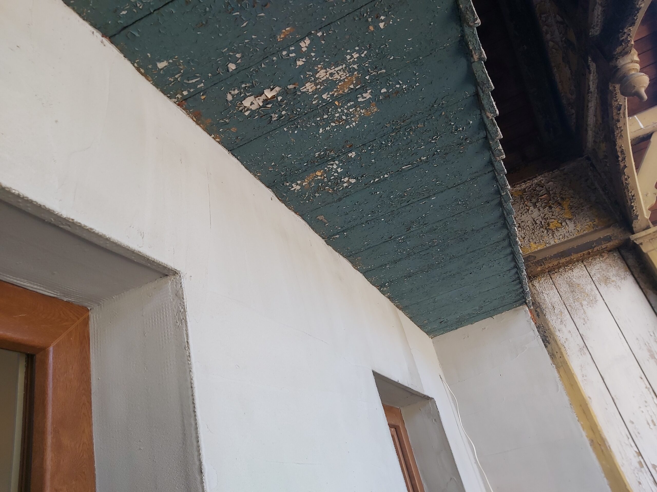 Korytarz z widocznym starym sufitem z drewnianych desek i łuszczącą się farbą, ściany po wstępnym odświeżeniu przygotowane do dalszych prac.