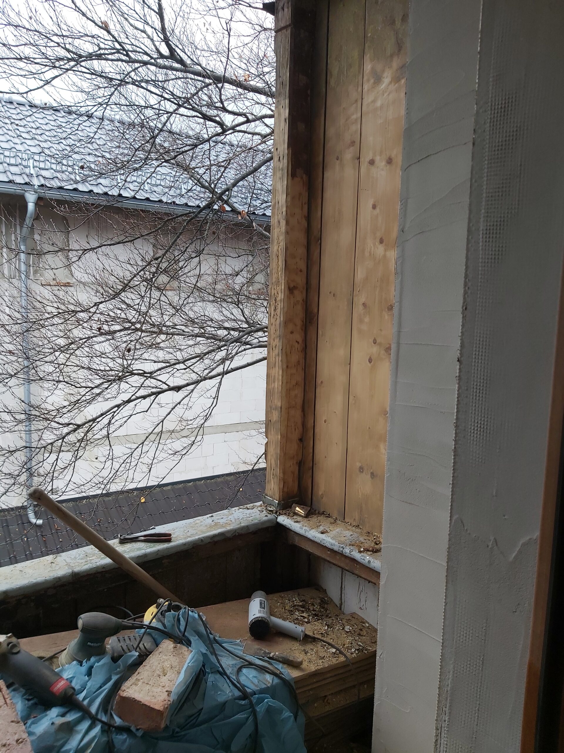 Ościeże okna z odsłoniętą drewnianą konstrukcją i prowadzonymi pracami remontowymi, widoczne narzędzia oraz przygotowanie do dalszego wykończenia.