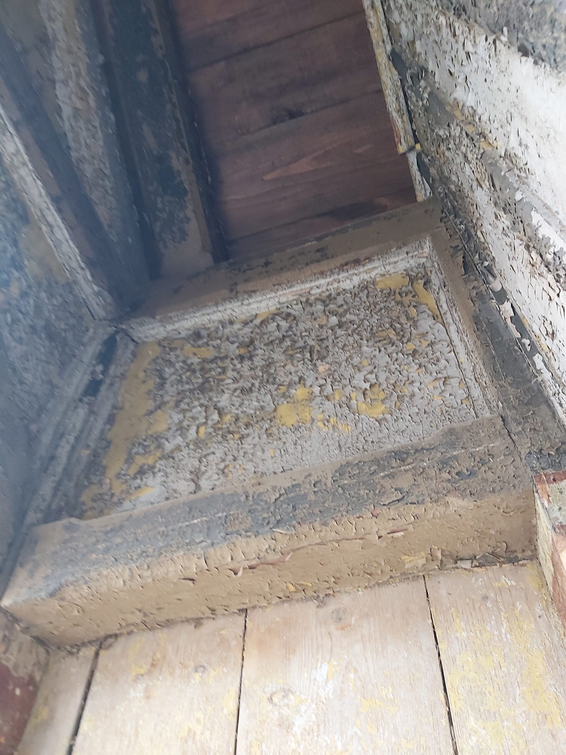 Zbliżenie na drewniany element konstrukcyjny balkonu z łuszczącą się farbą i widocznym osypującym się tynkiem przed pracami renowacyjnymi.