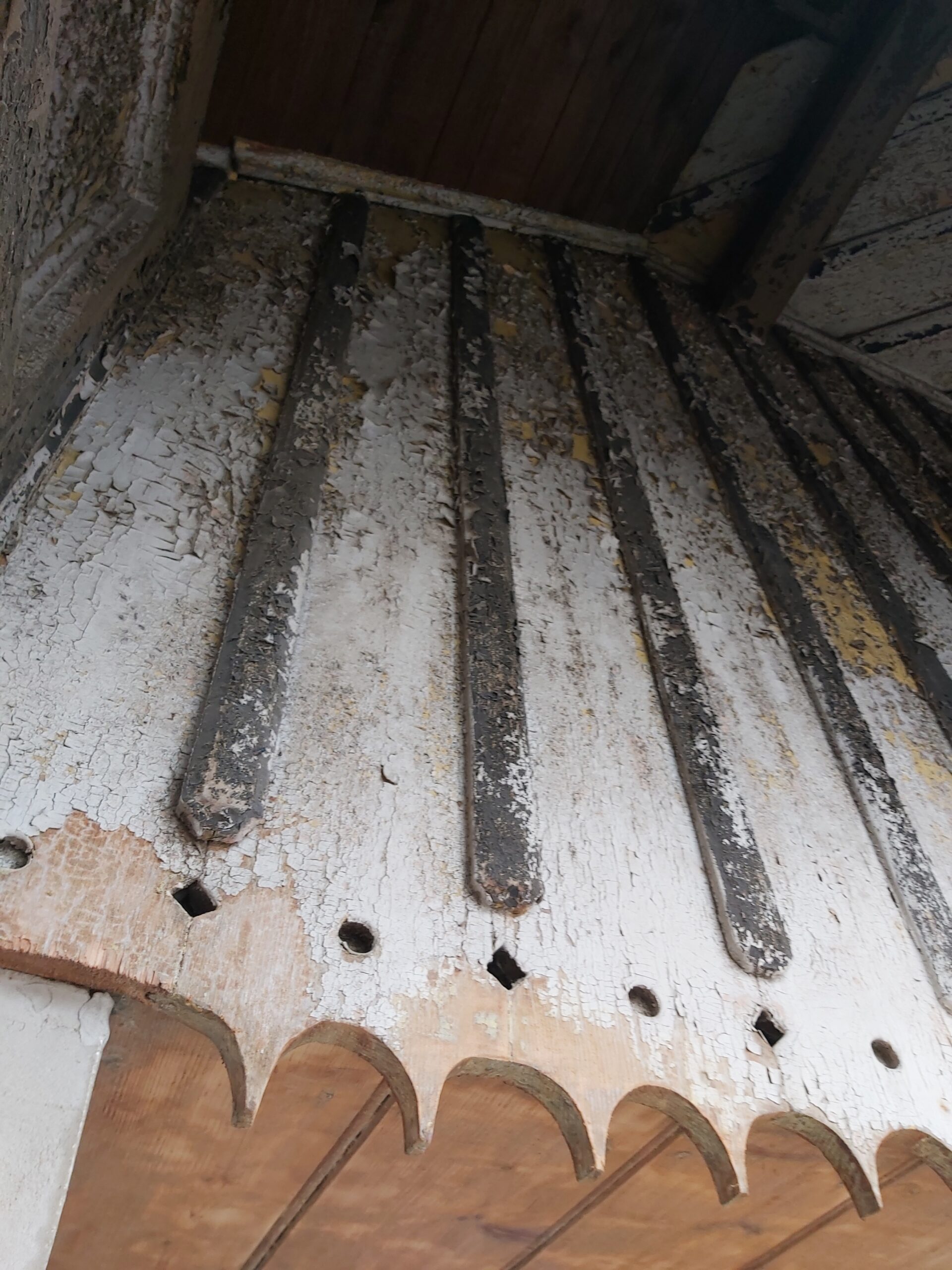 Fragment starej drewnianej podbitki balkonu z pionowymi listwami i mocno łuszczącą się warstwą farby przed renowacją.