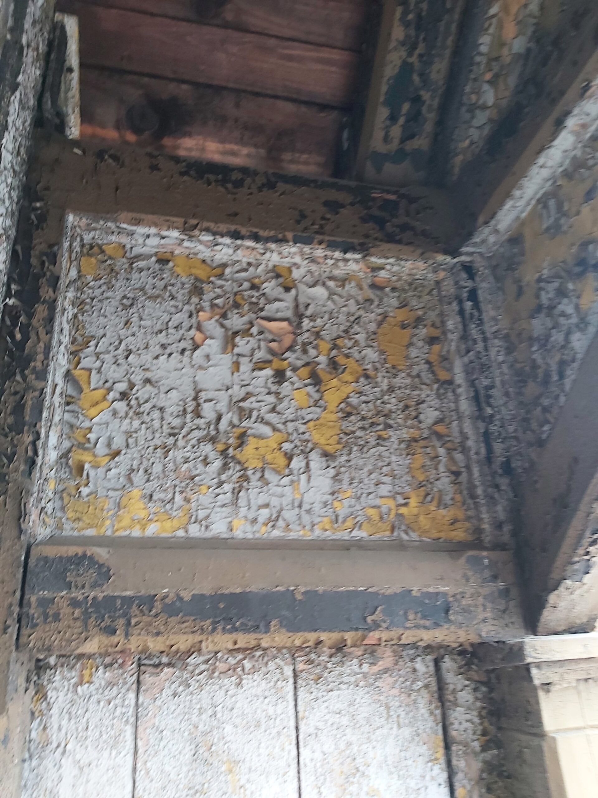 Fragment drewnianej konstrukcji balkonu z mocno łuszczącą się farbą oraz widocznymi śladami degradacji materiału przed renowacją.