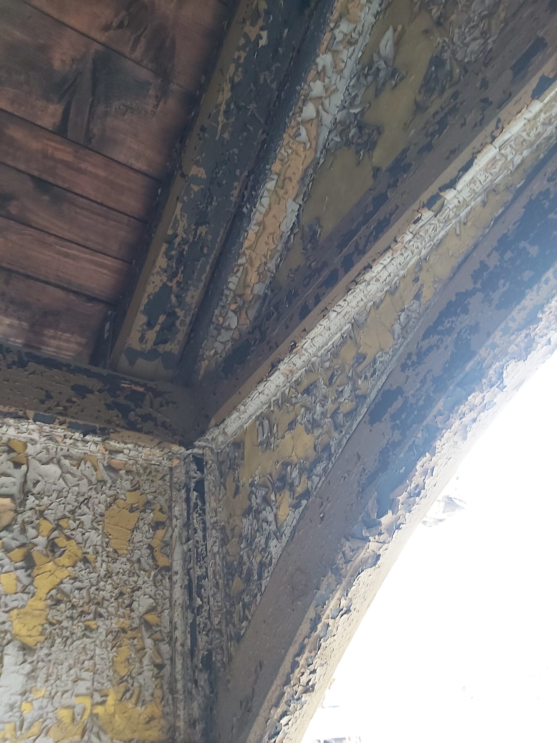 Detal drewnianych belek i deskowania balkonu z łuszczącą się farbą oraz widocznymi oznakami wieloletniego zużycia przed remontem.