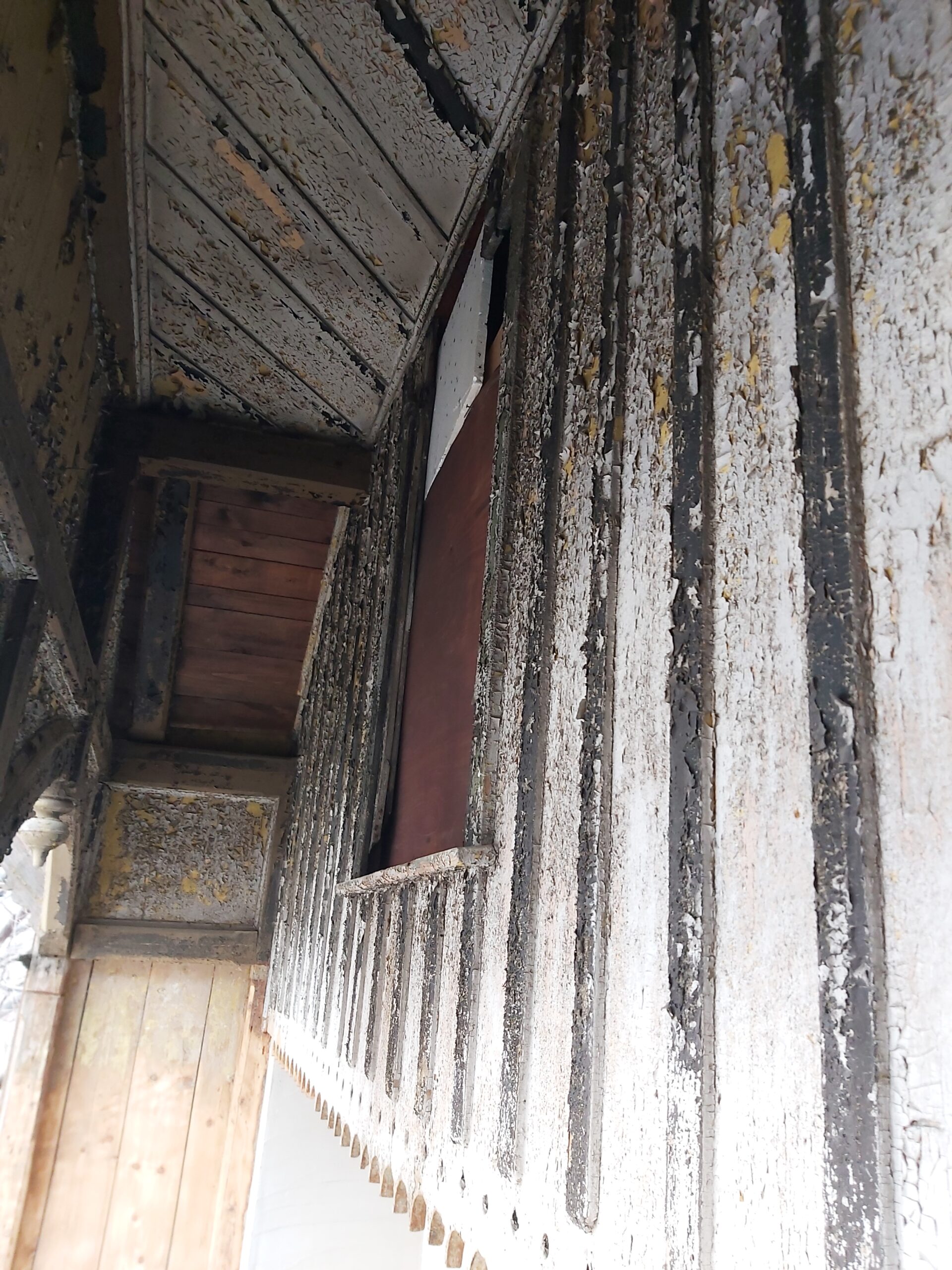 Zniszczona drewniana elewacja z pionowymi deskami i łuszczącą się farbą, widoczny stan techniczny przed pracami remontowymi.