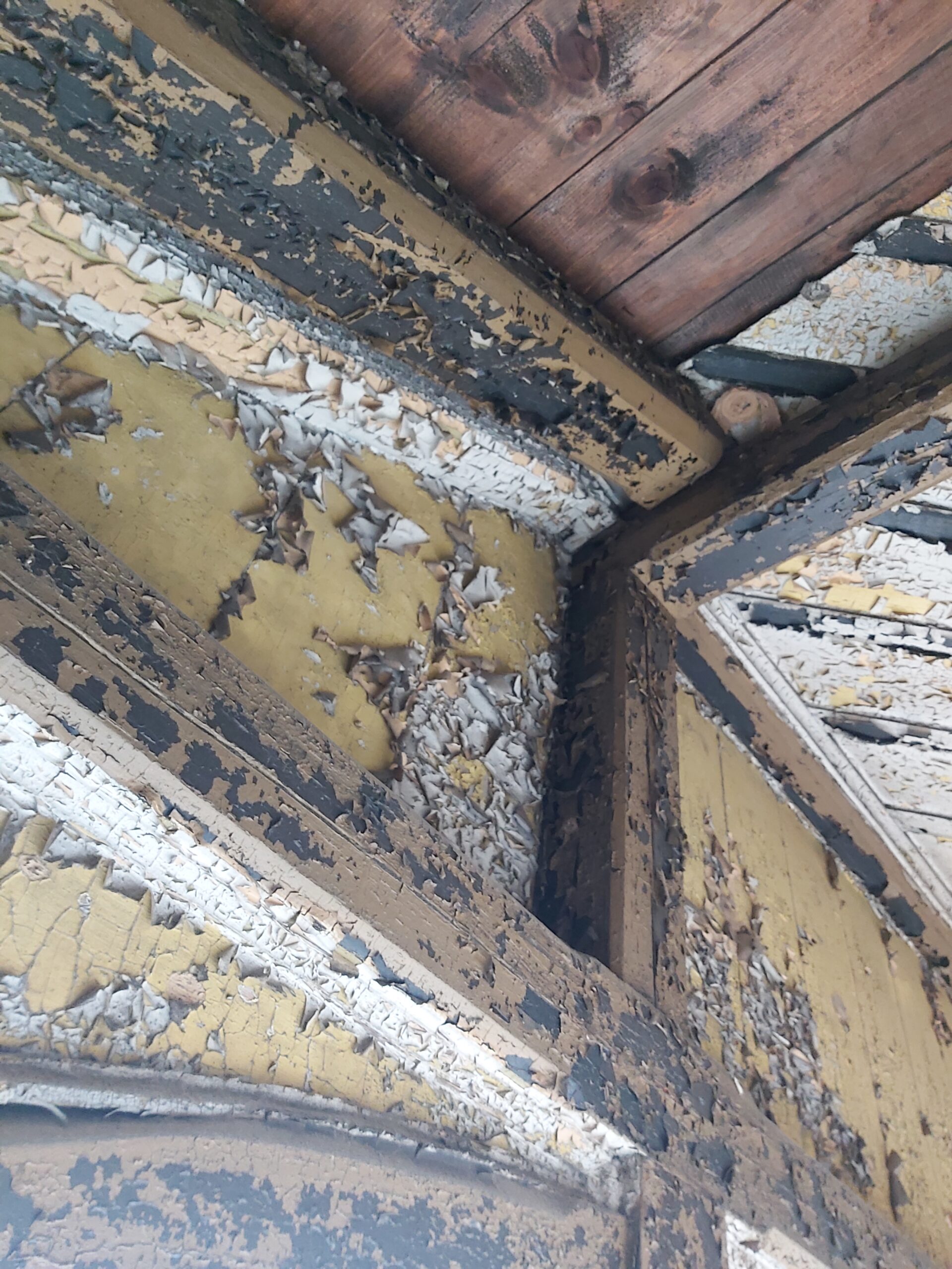 Fragment starej drewnianej konstrukcji pod dachem z łuszczącą się farbą i widocznym zużyciem materiału, stan przed remontem.