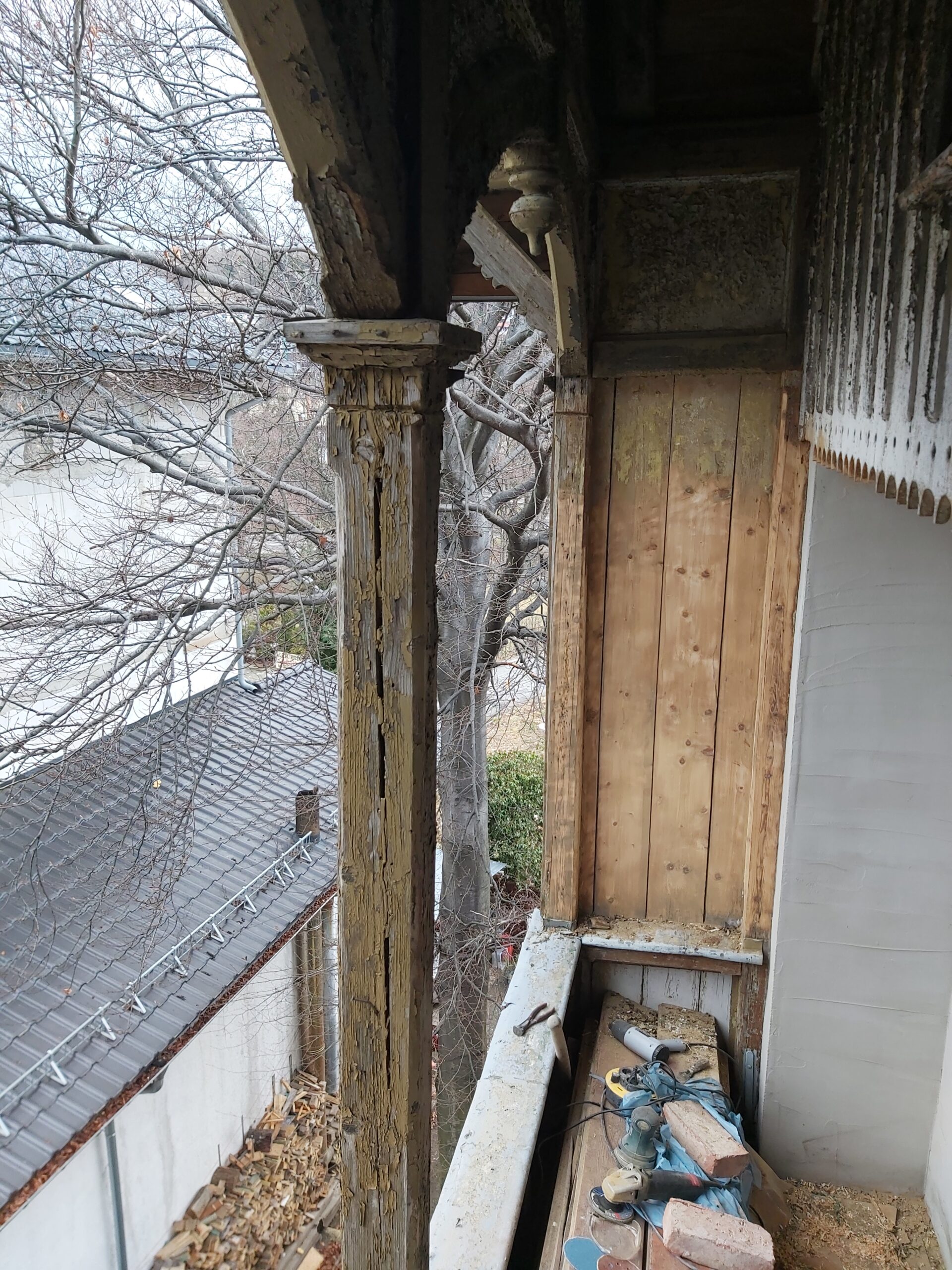 Stary drewniany słup balkonu z mocno łuszczącą się farbą i śladami degradacji drewna, widok podczas prac remontowych.