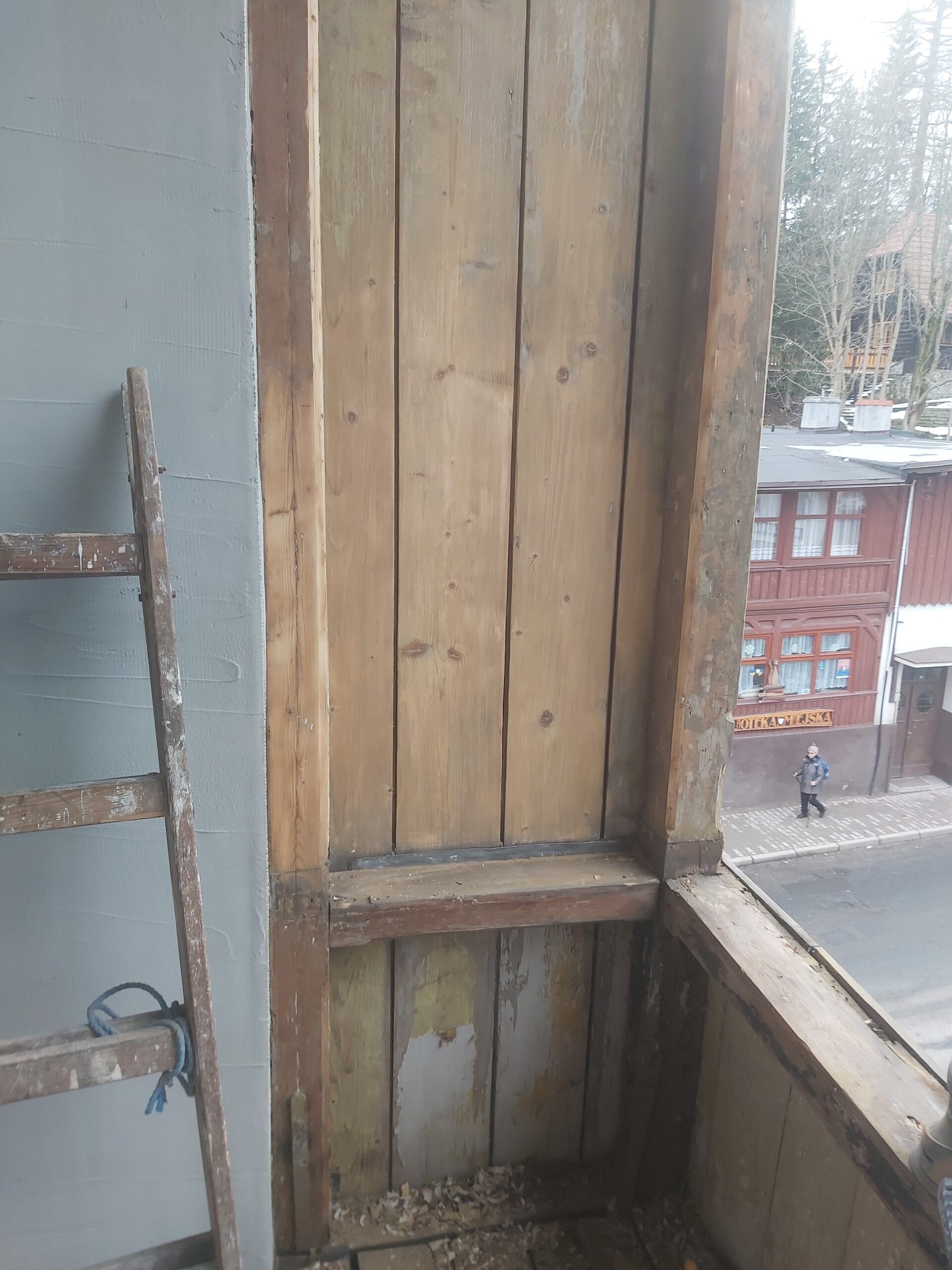 Oczyszczona pionowa zabudowa balkonu z naturalnych drewnianych desek i belki konstrukcyjnej, przygotowana do dalszych prac renowacyjnych.