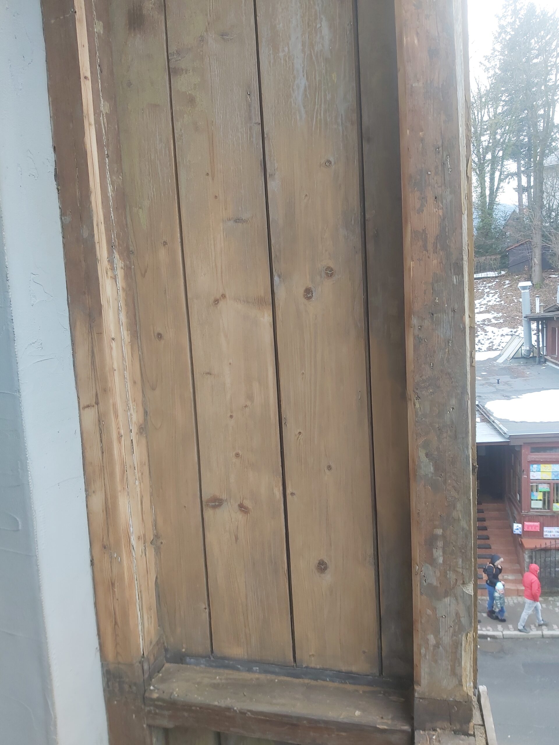 Oczyszczona drewniana wnęka balkonu z widocznymi deskami i śladami wcześniejszych warstw wykończenia, przygotowana do dalszych prac renowacyjnych.