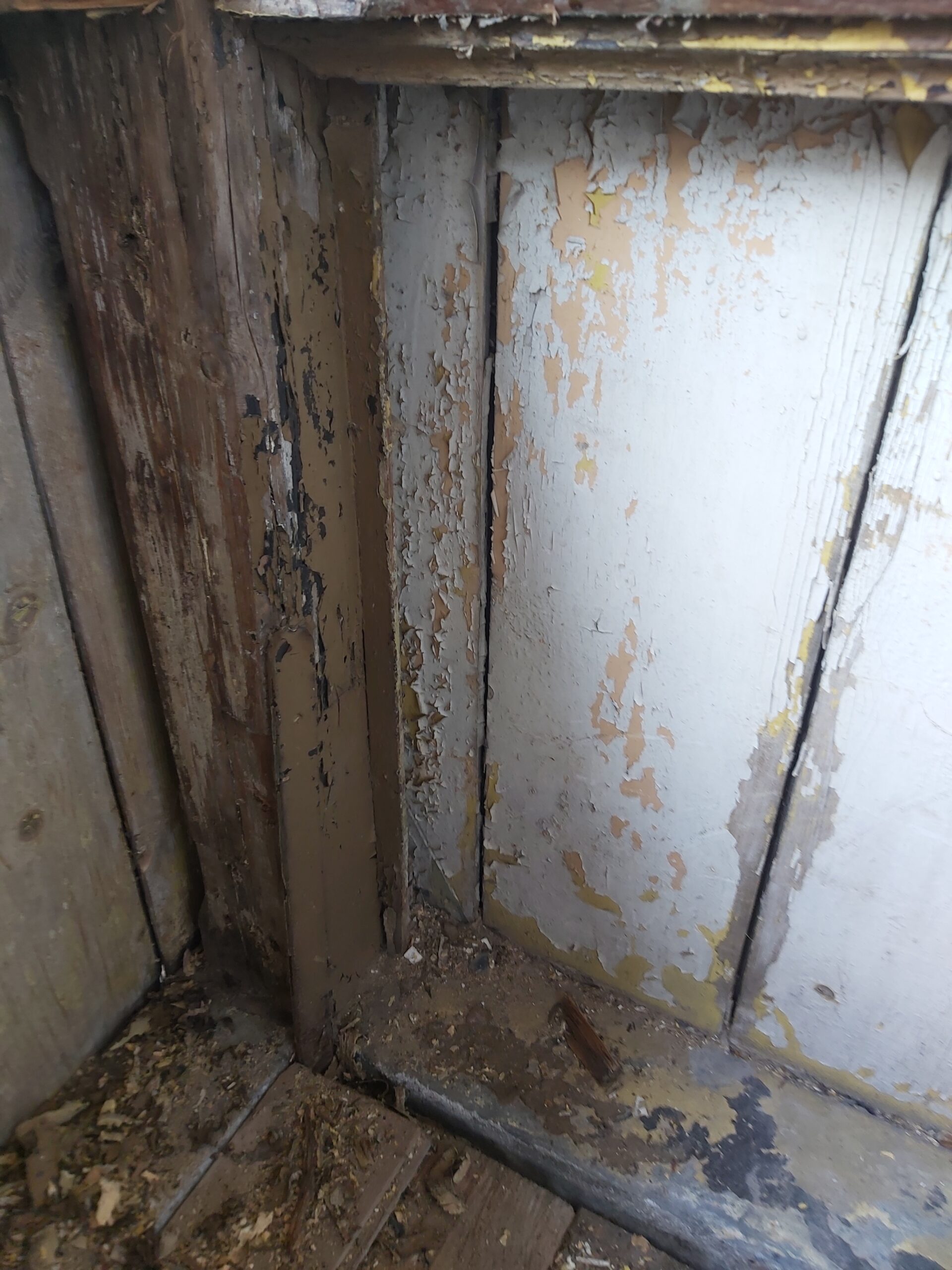 Fragment starej ściany balkonu z pionowymi deskami, odpadającą farbą i widocznymi śladami zużycia drewna przed rozpoczęciem prac renowacyjnych.