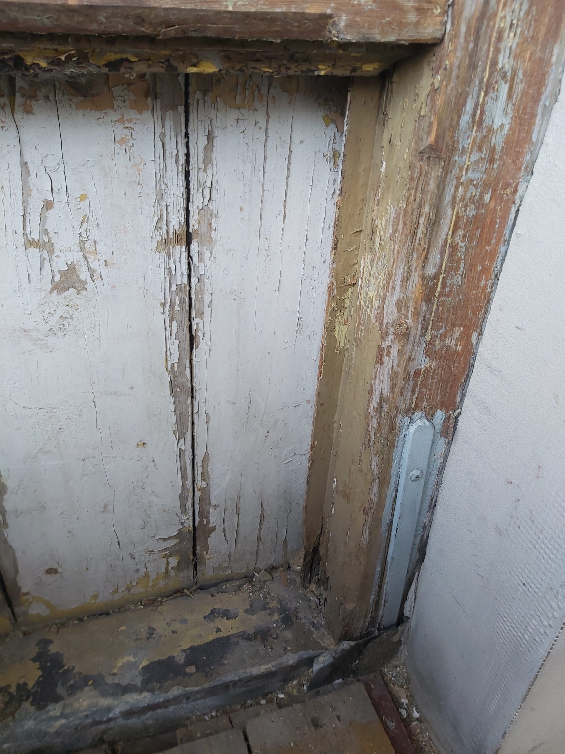 Zbliżenie na stare, spękane deski oraz narożny drewniany słup balkonu z łuszczącą się farbą i śladami zużycia przed pracami remontowymi.