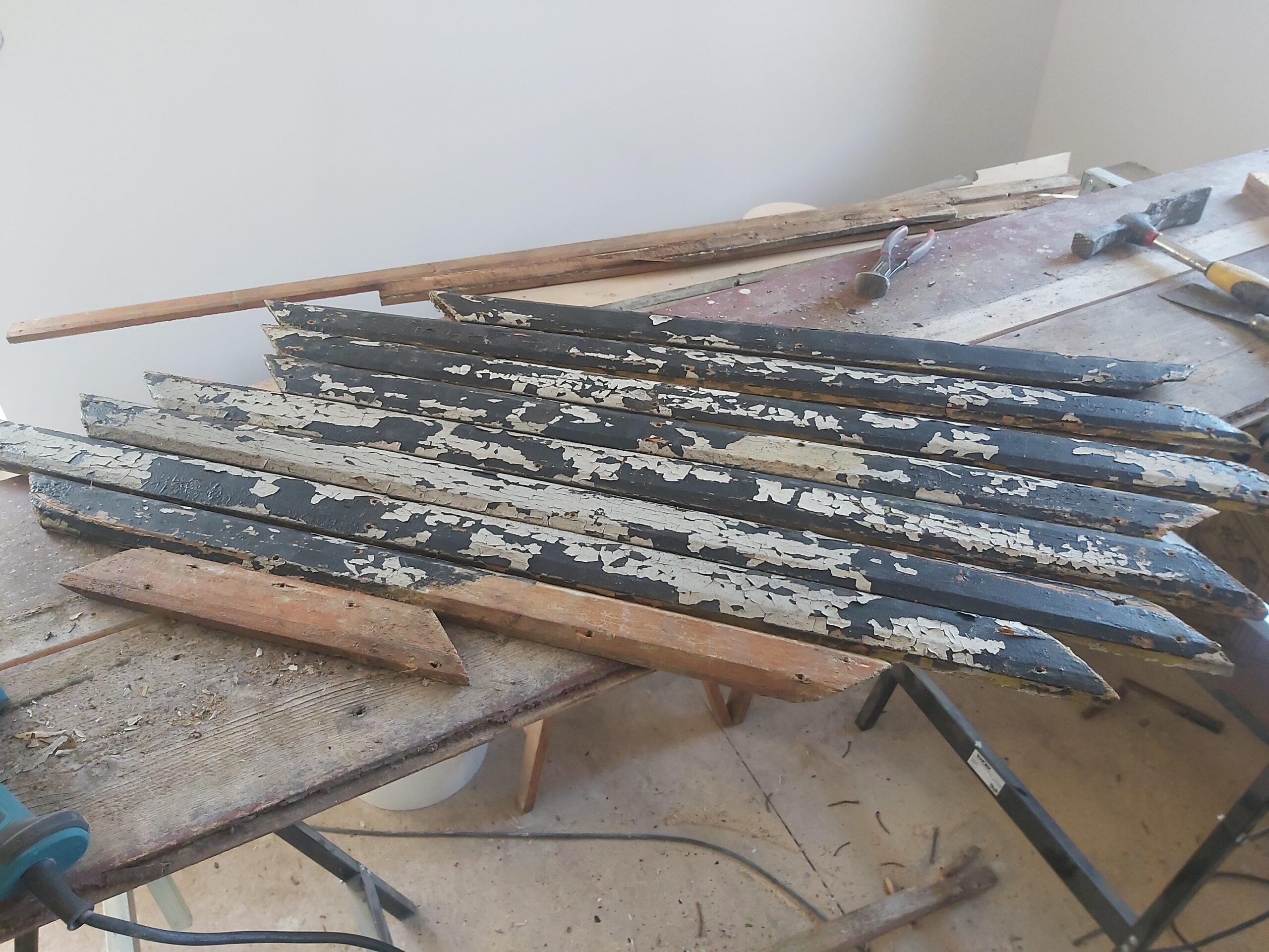 Zdemontowane stare drewniane listwy balkonowe z łuszczącą się farbą, ułożone na stole roboczym podczas prac remontowych.