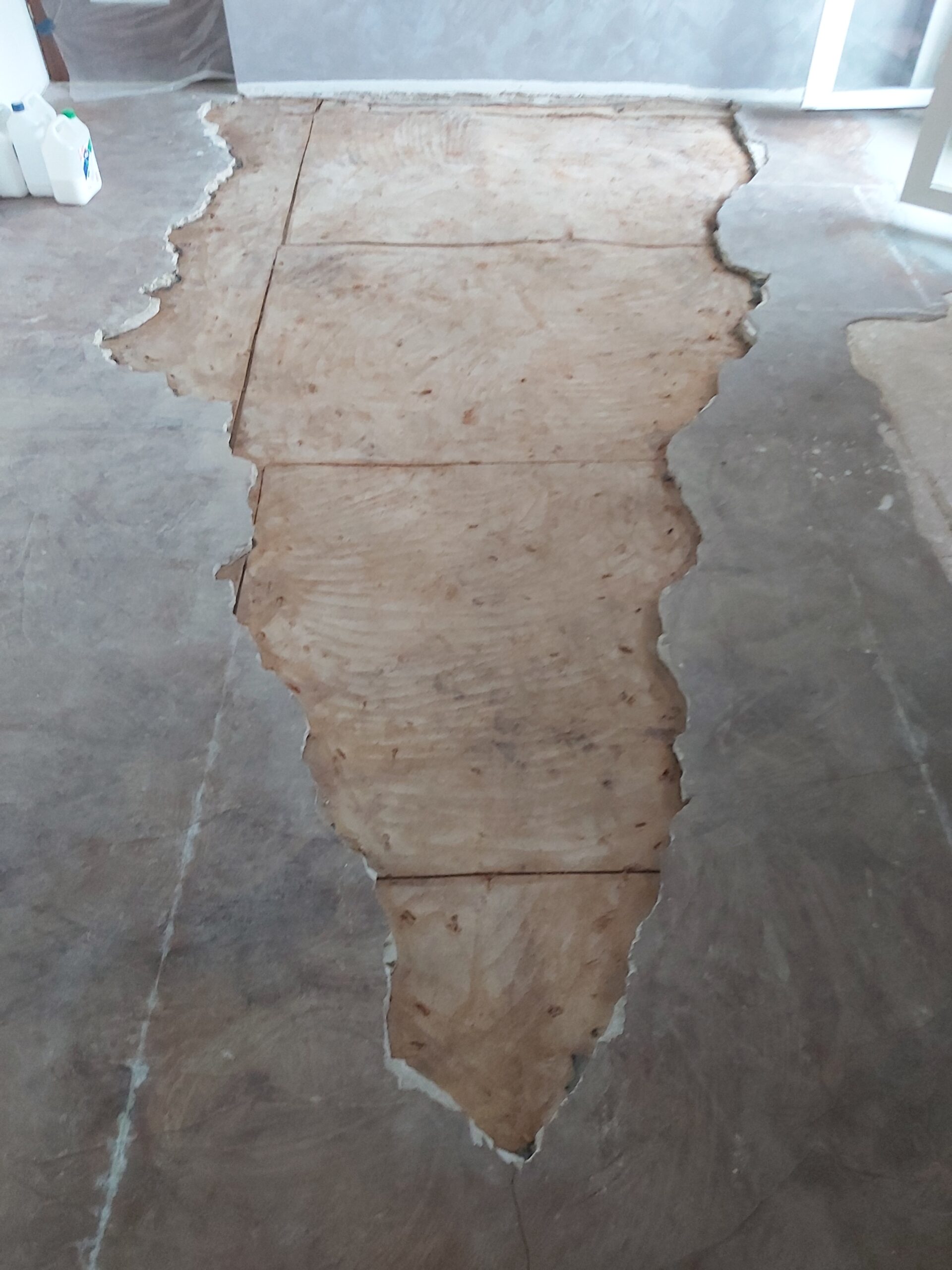 Centralna część podłogi z odsłoniętą płytą konstrukcyjną po usunięciu starej posadzki, otoczona pozostałościami wcześniejszych warstw w trakcie remontu.