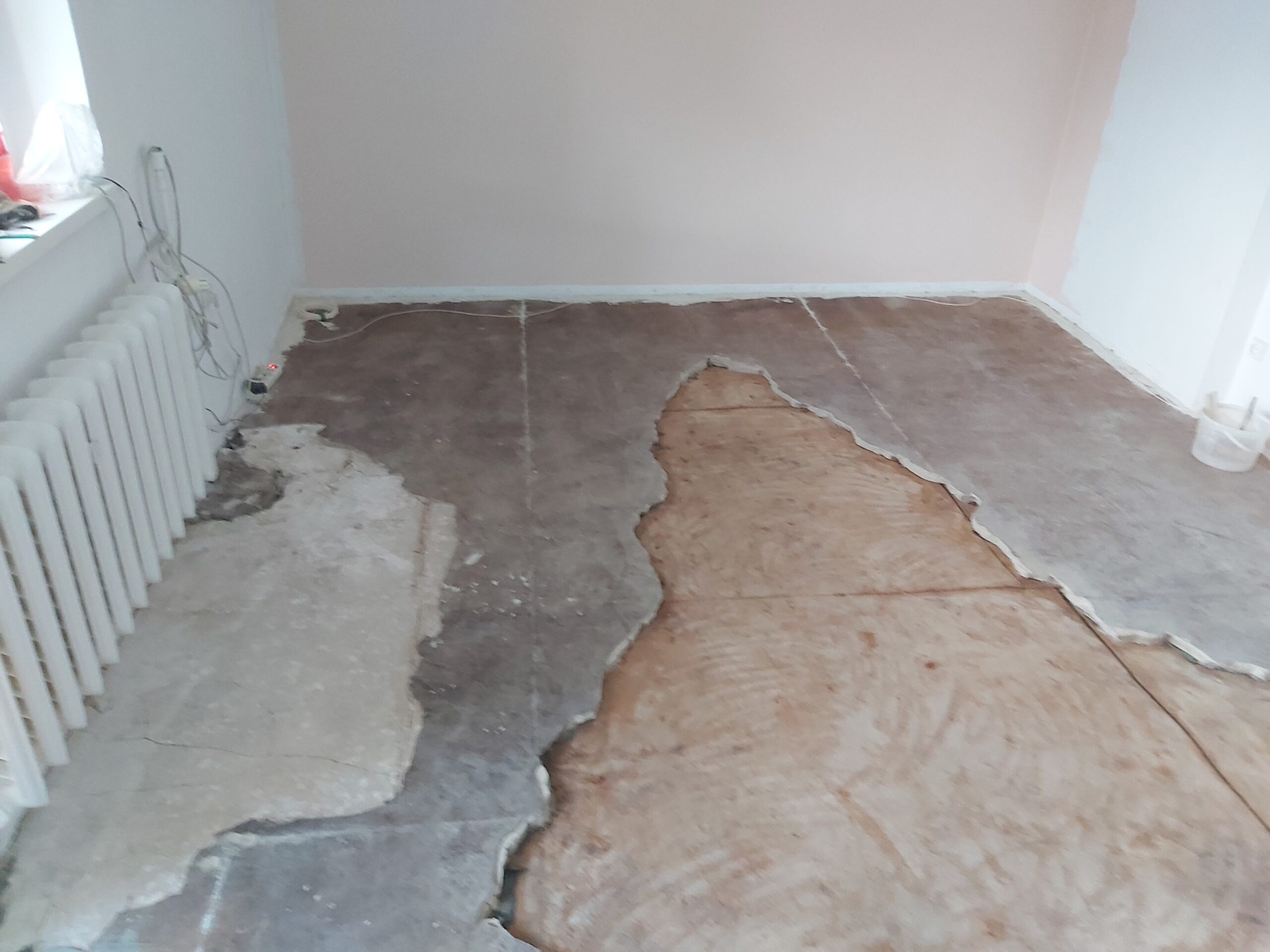 Fragment podłogi po usunięciu starej posadzki, z widocznymi różnymi warstwami podłoża i odsłoniętą powierzchnią betonu w trakcie remontu.