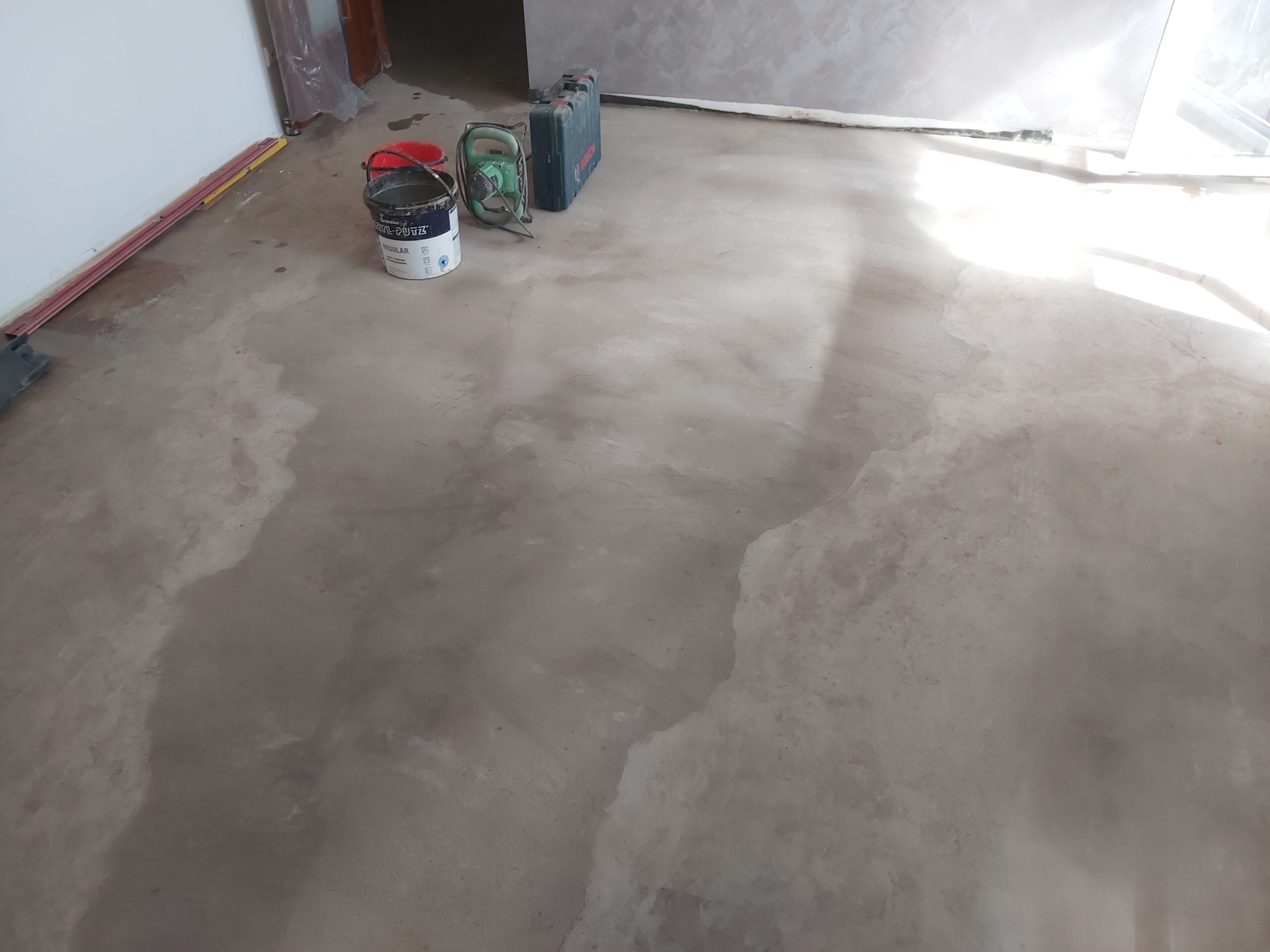 Wyrównana posadzka cementowa w pomieszczeniu, z widocznymi narzędziami i materiałami budowlanymi przygotowanymi do dalszych prac.