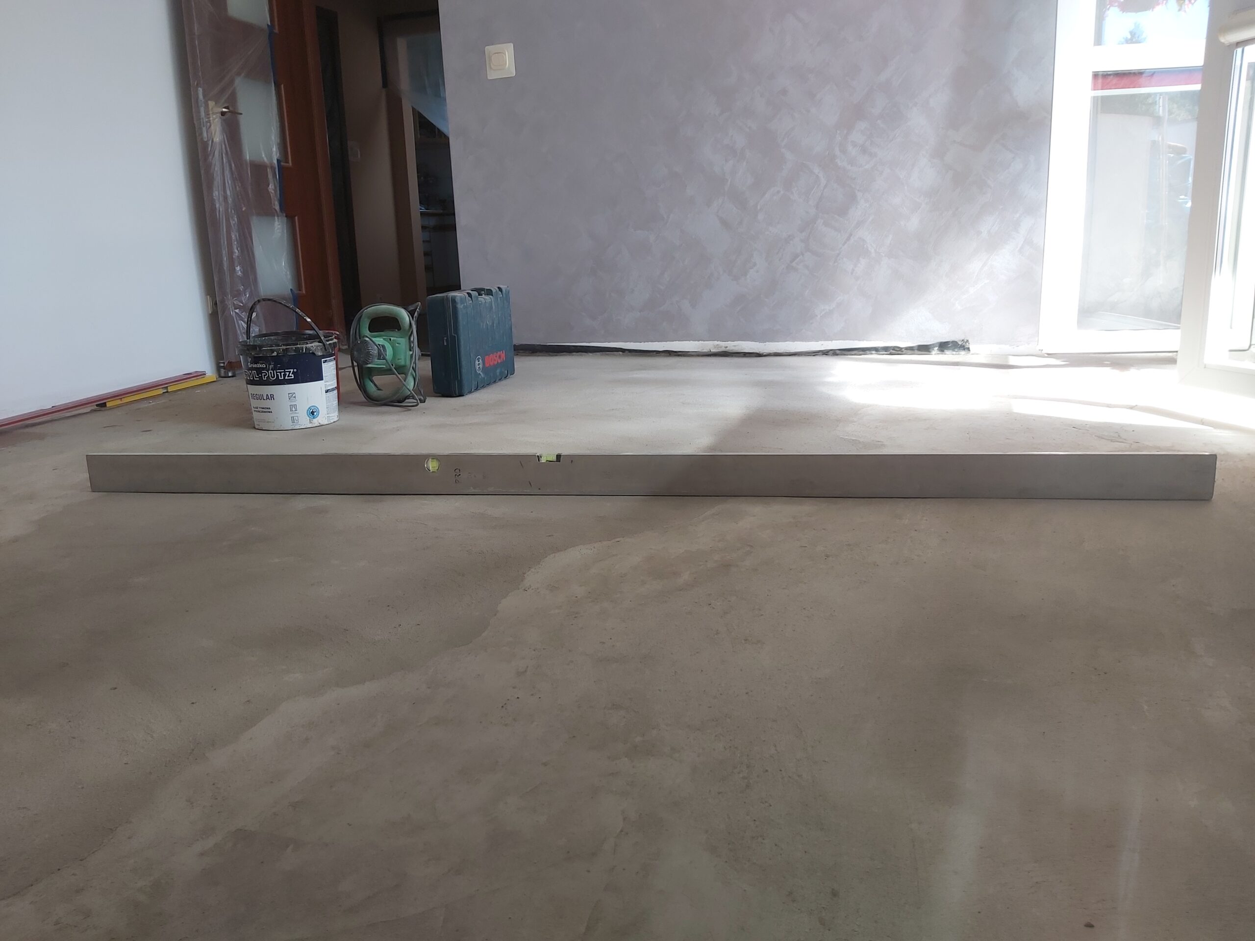 Kontrola równości świeżej posadzki za pomocą długiej poziomicy w pomieszczeniu mieszkalnym.