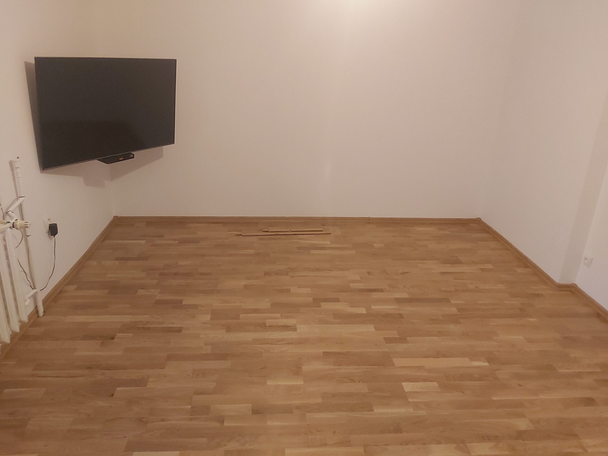 Pusty salon z wykończoną drewnianą podłogą i telewizorem zamontowanym na ścianie.