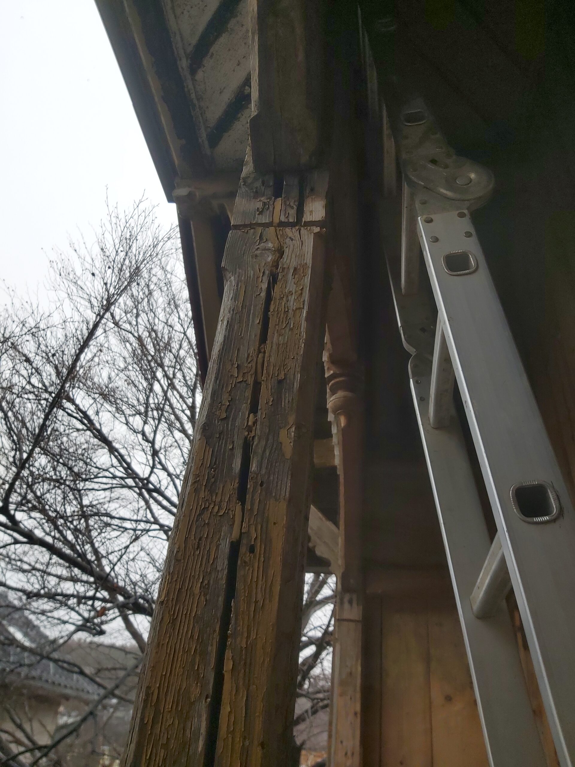 Pęknięty i spróchniały drewniany słup nośny balkonu z widocznymi śladami wieloletniego zawilgocenia i degradacji drewna.